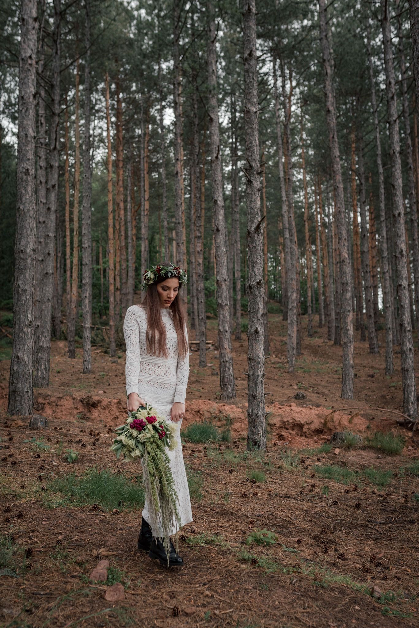A dreamy forest scene with someone in a flowing white dress holding a rustic bouquet among tall pine trees.