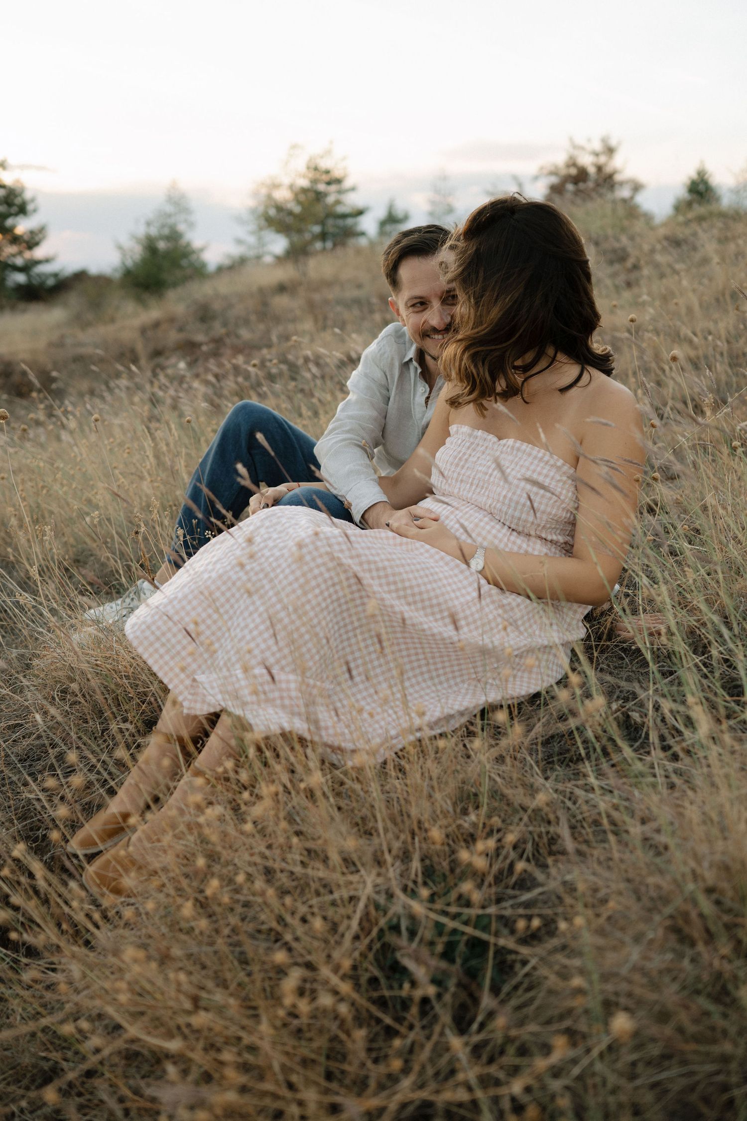 A couple shares an intimate moment while lying in a golden grassy field during sunset.