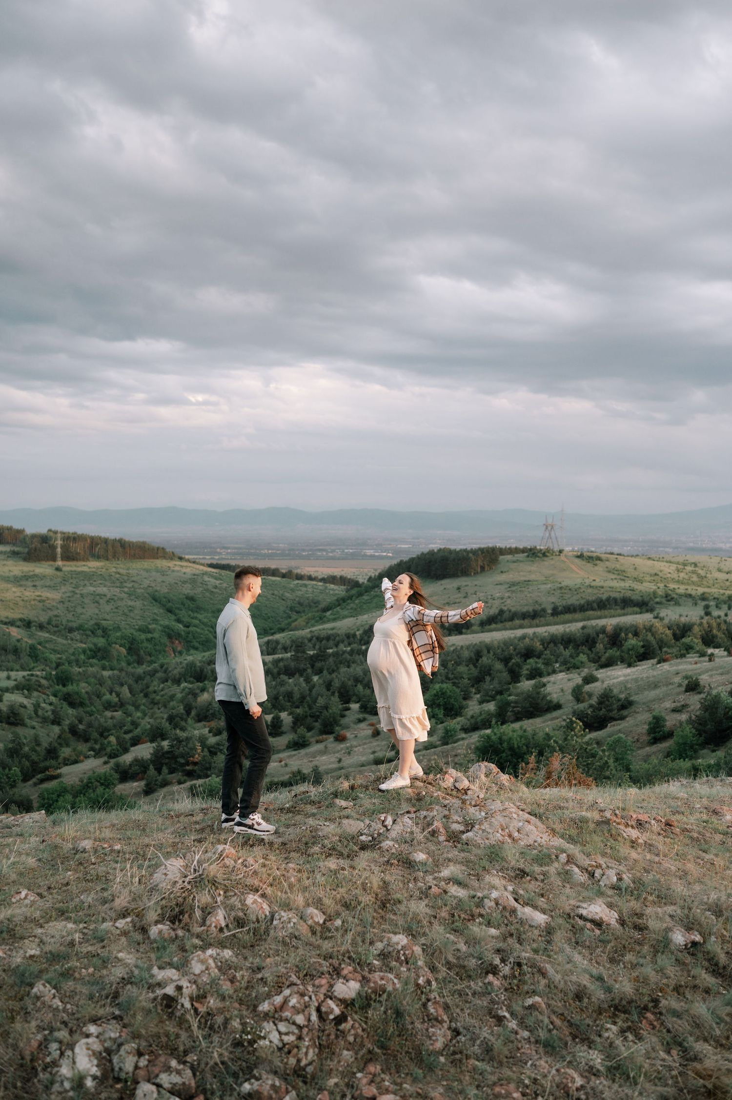 People explore a scenic hilltop overlooking rolling landscapes under dramatic cloudy skies.