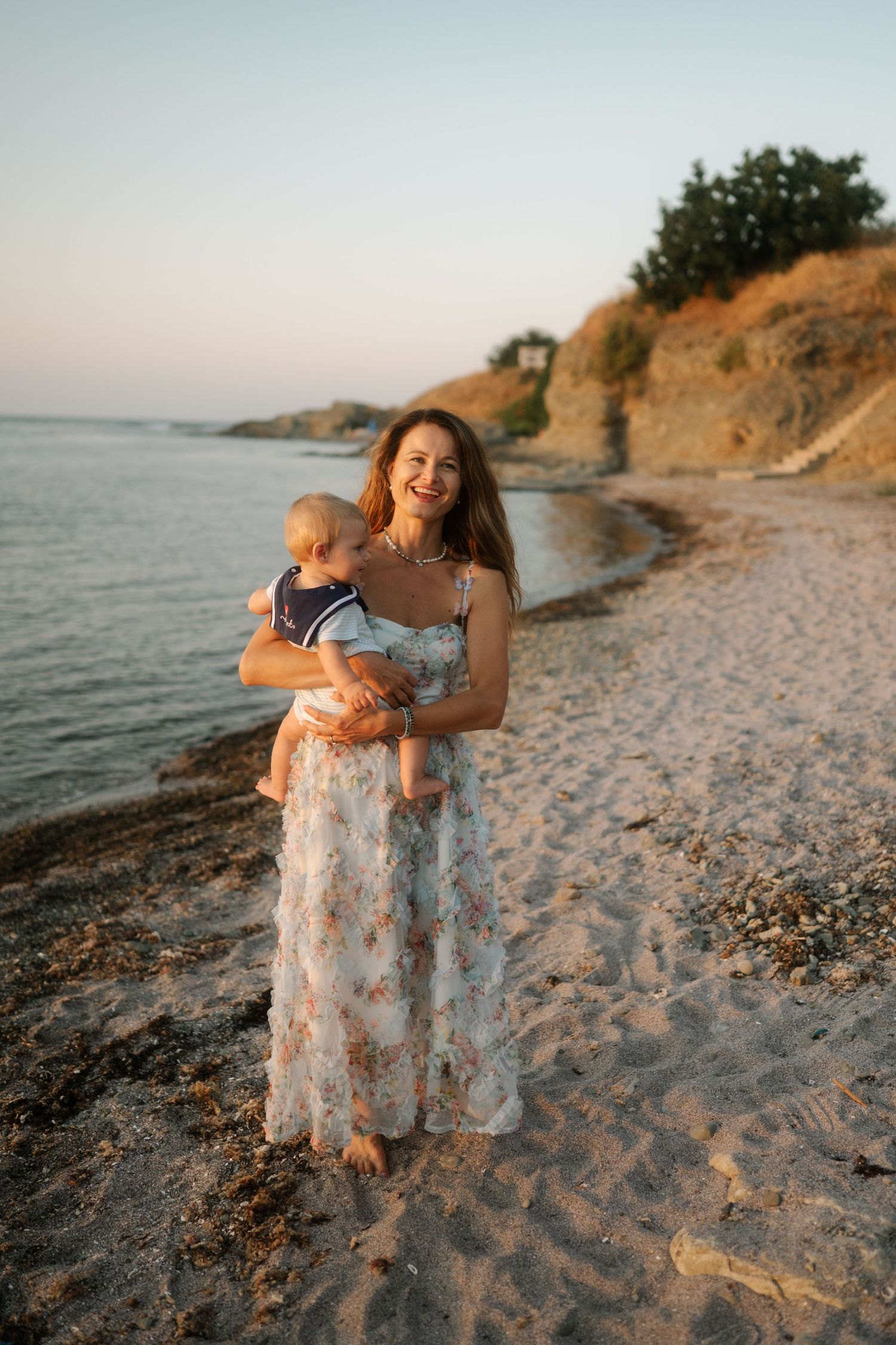 A tender moment shared between two people on a sandy beach at sunset with cliffs and ocean in the background.