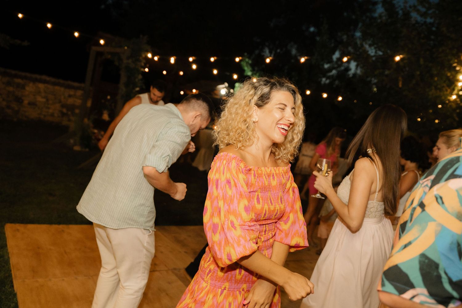 People dancing together under string lights at an outdoor evening party celebration.