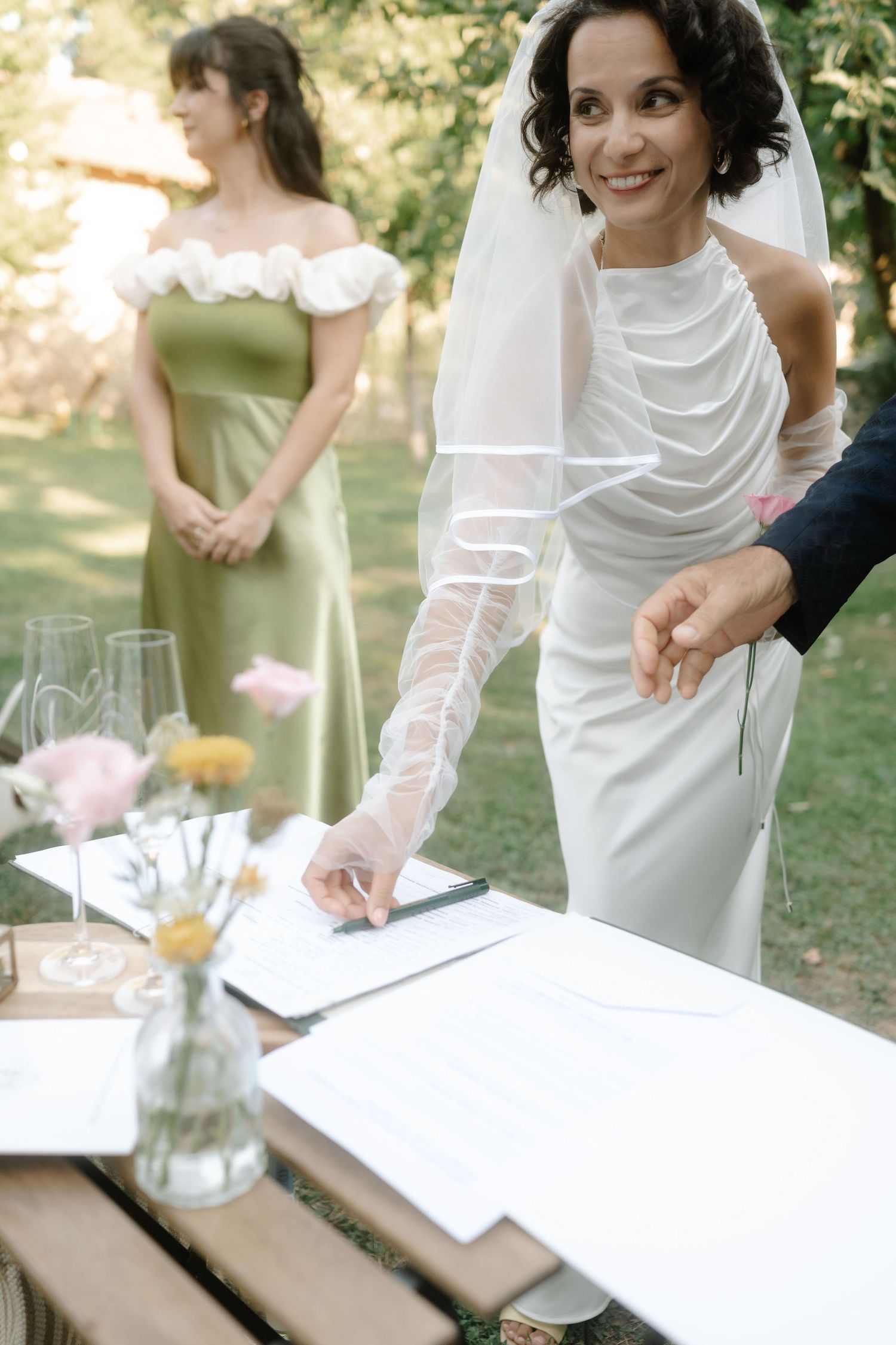 People in formal attire gather around a white table at an outdoor event pouring drinks and celebrating together.