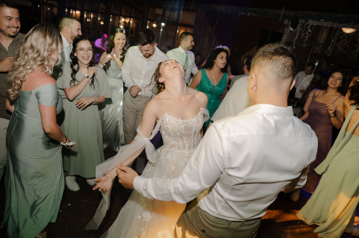 Wedding reception guests enjoying themselves while dancing in a dimly lit venue with festive lighting.