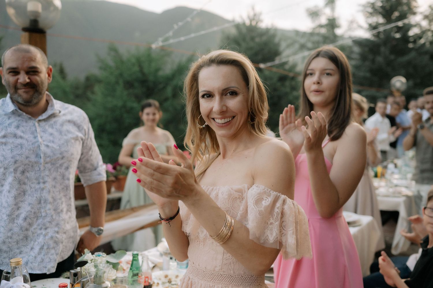 Wedding guests celebrate outdoors at a scenic mountain reception venue during sunset with drinks and dancing.