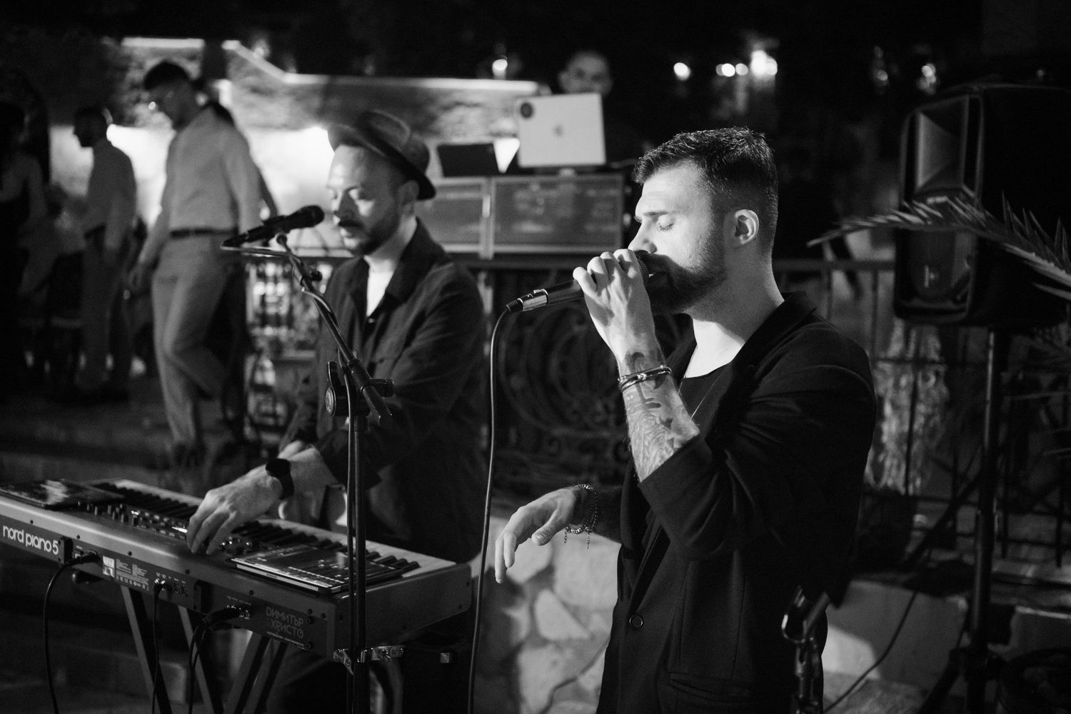 Musicians perform on stage in a dimly lit venue with instruments and microphones visible.