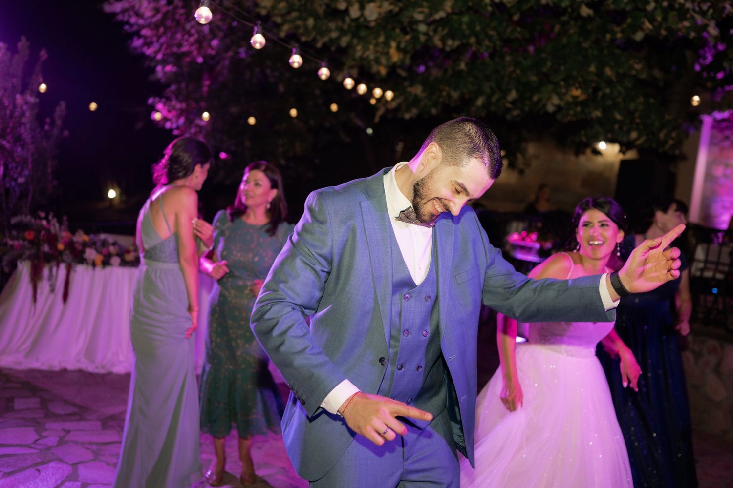 Couples dancing together at an outdoor evening wedding reception illuminated by string lights and purple lighting.