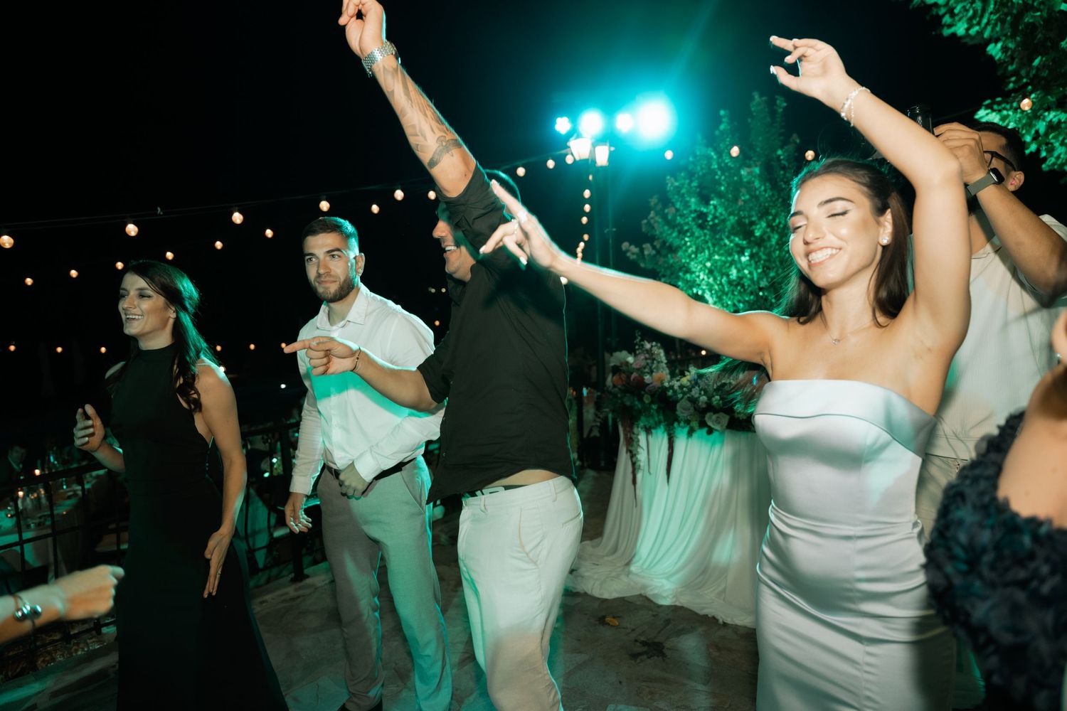 People dancing and celebrating at a nighttime outdoor party with green lighting and festive atmosphere.
