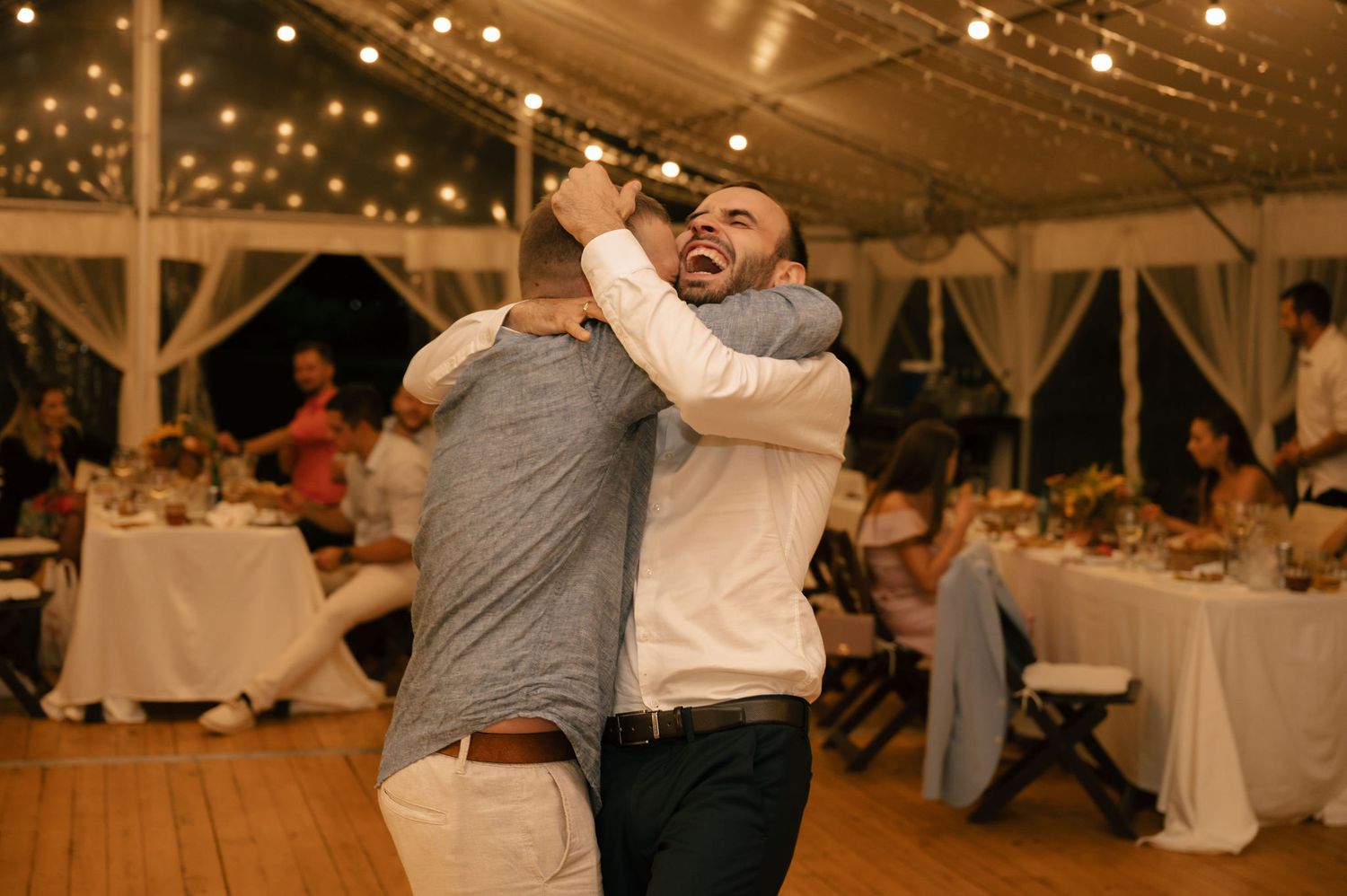 Couples dancing together at an elegant wedding reception under warm glowing lights in a rustic barn venue.