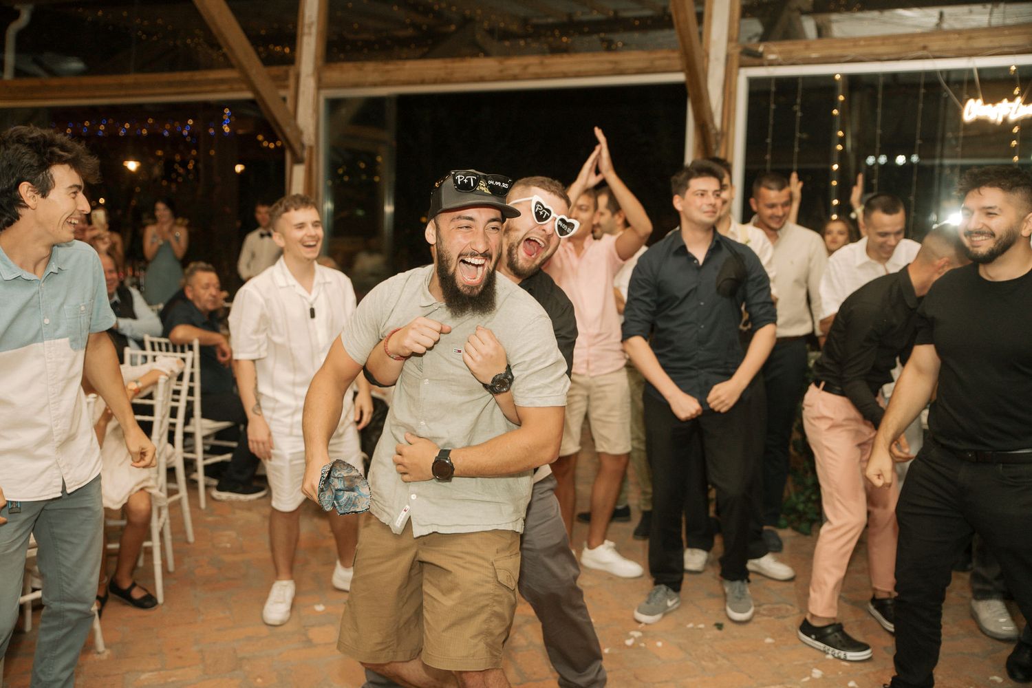 People dancing and celebrating at a lively wedding reception on a wooden dance floor.