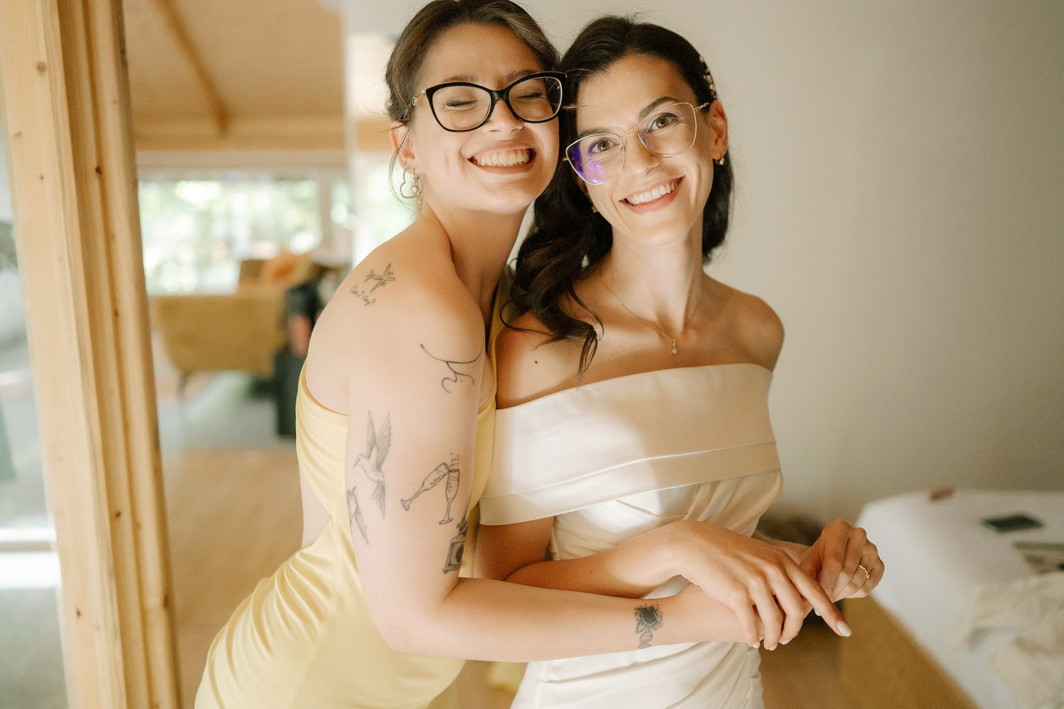 Two people embrace in a warm moment while wearing formal attire in a sunlit room.