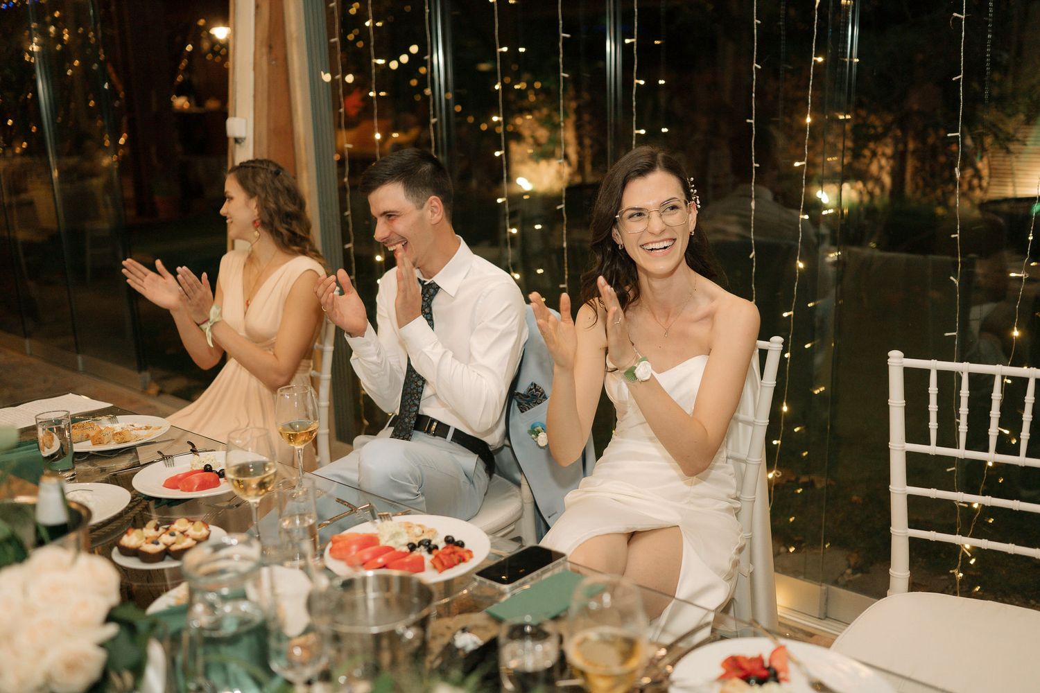 Wedding reception guests enjoying dinner and conversation at elegantly decorated tables in a dimly lit venue.