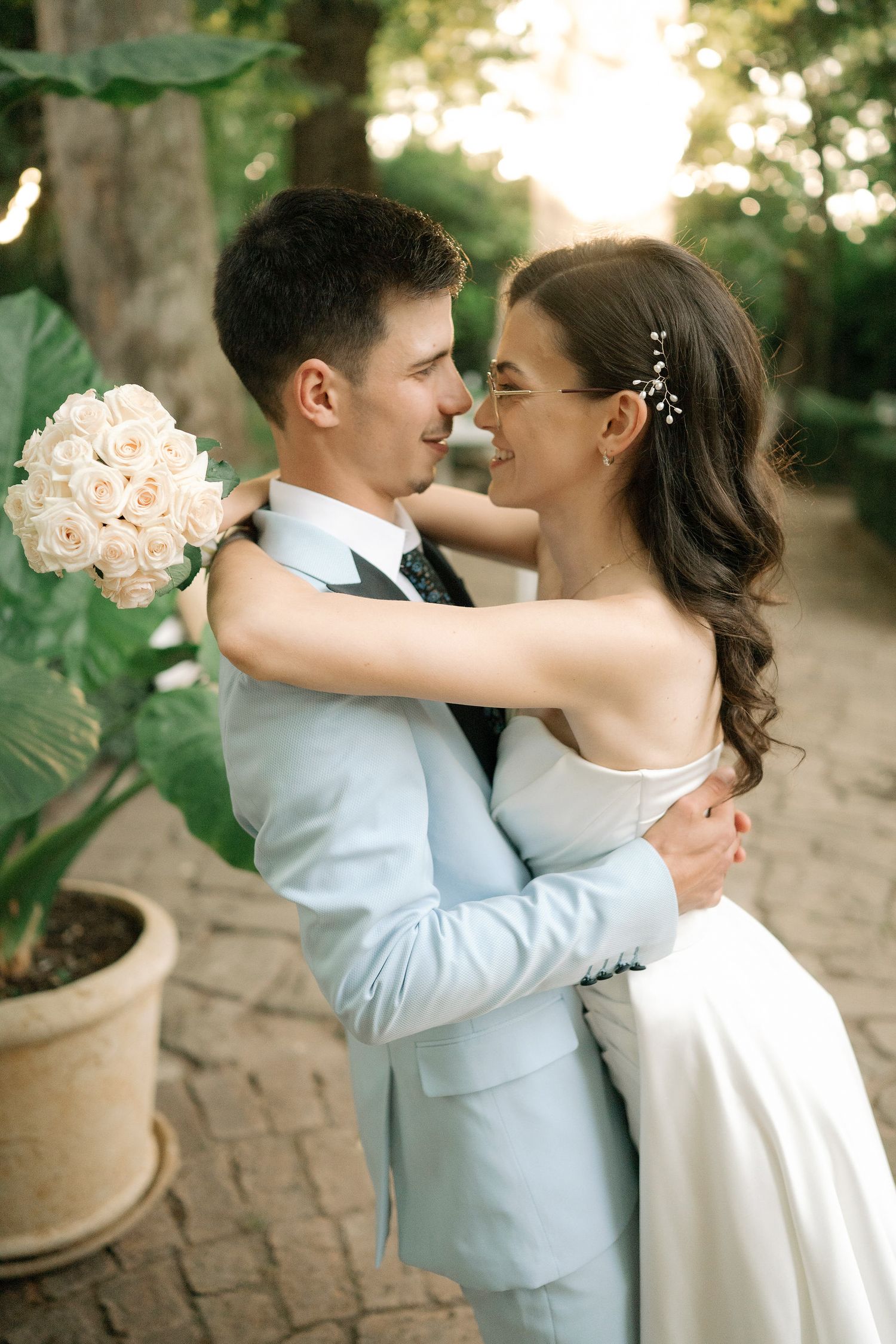 Romantic wedding couple embraces and shares intimate moments in a garden setting with blush pink bouquet.