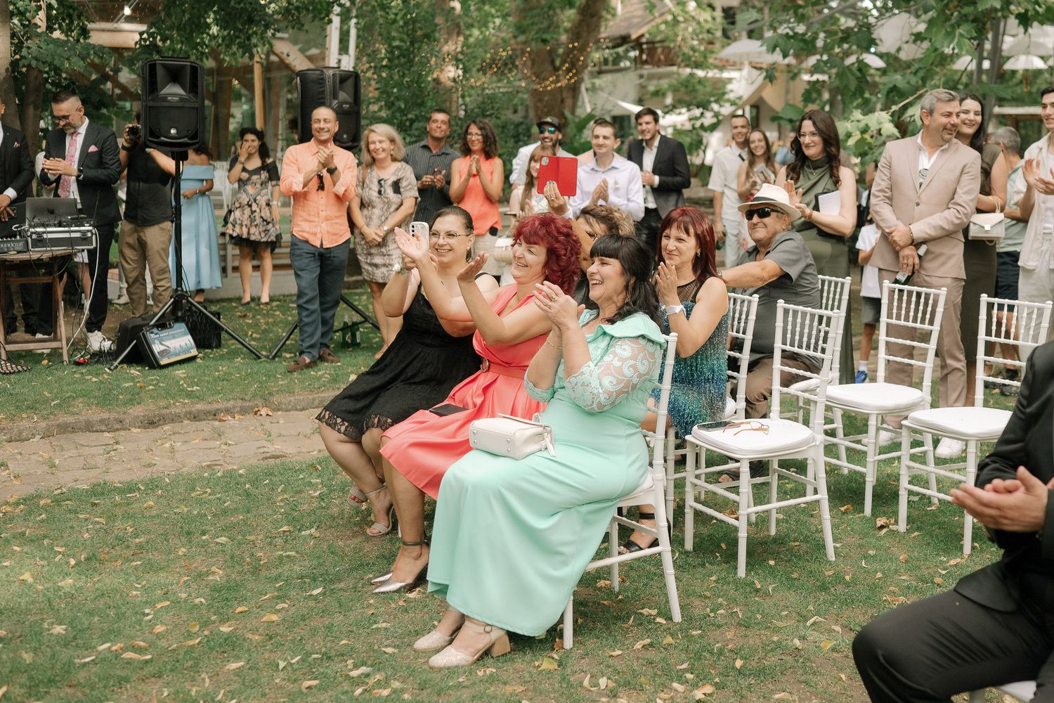 Wedding guests dance and celebrate together on a grassy lawn during an outdoor garden reception.
