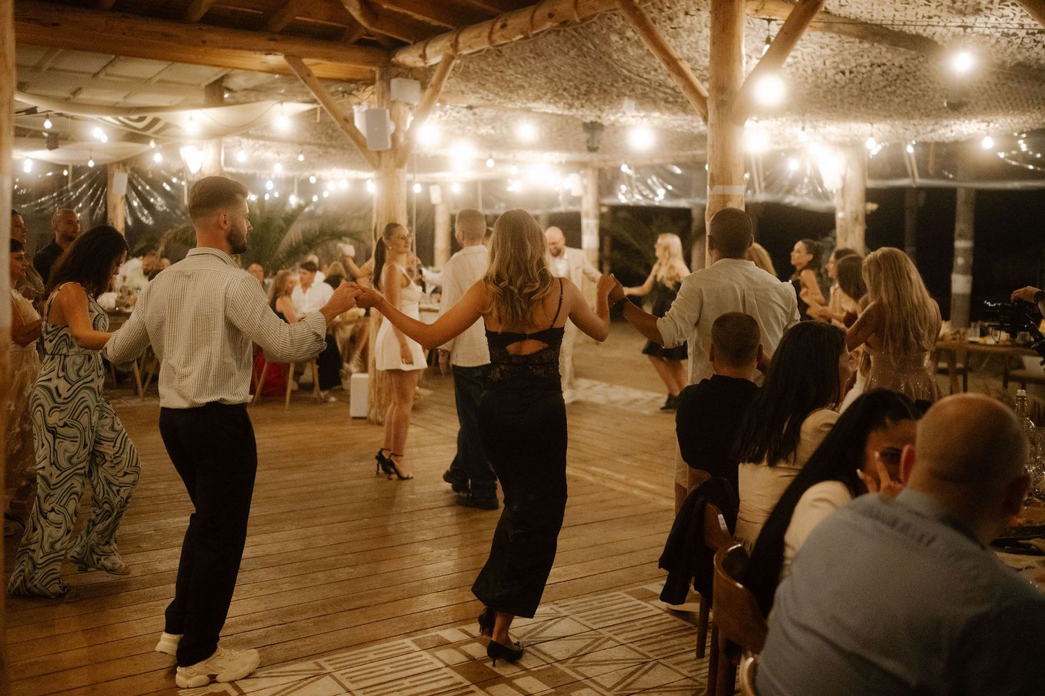 People dancing in pairs at a rustic barn venue illuminated by warm string lights during an evening celebration.