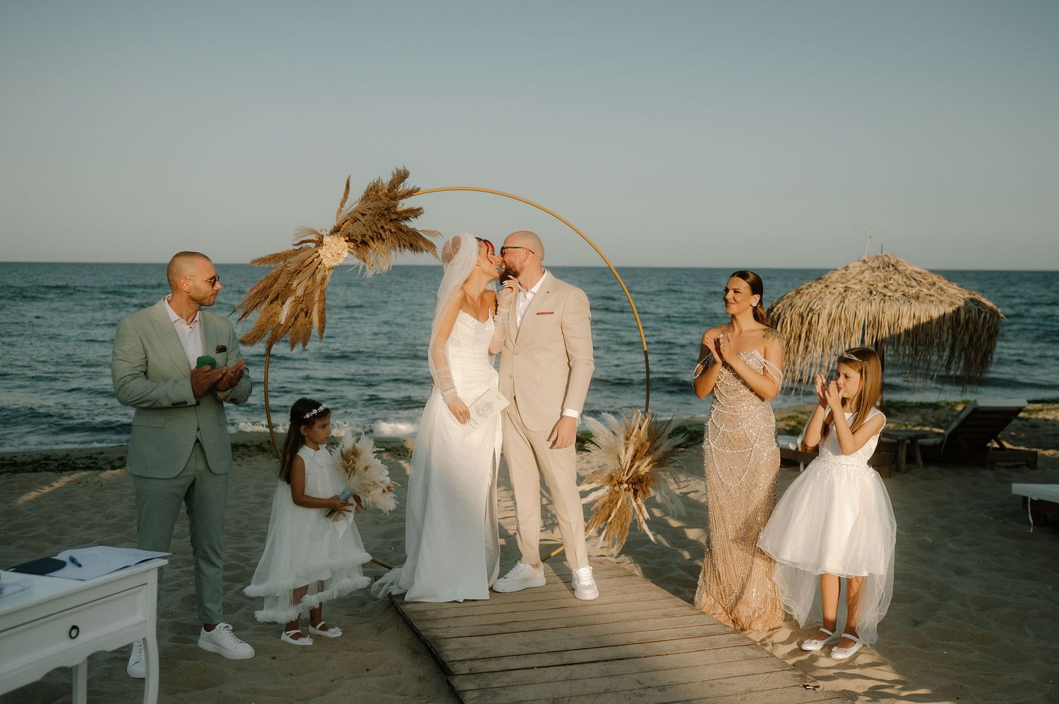 Wedding party celebrates on a wooden pier by the ocean at sunset with wind blowing through their hair.