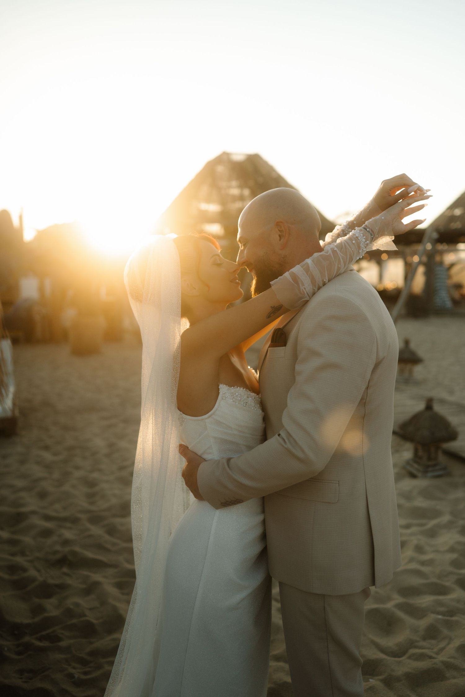 Romantic beach wedding photoshoot at sunset with couple embracing on sandy shore.