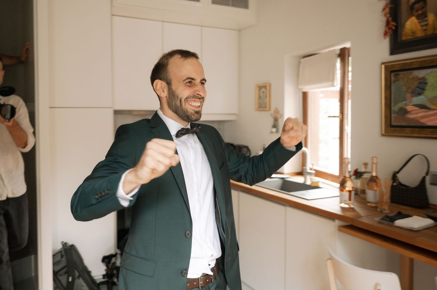 A person in a dark suit jacket gestures animatedly while speaking in a bright indoor space.