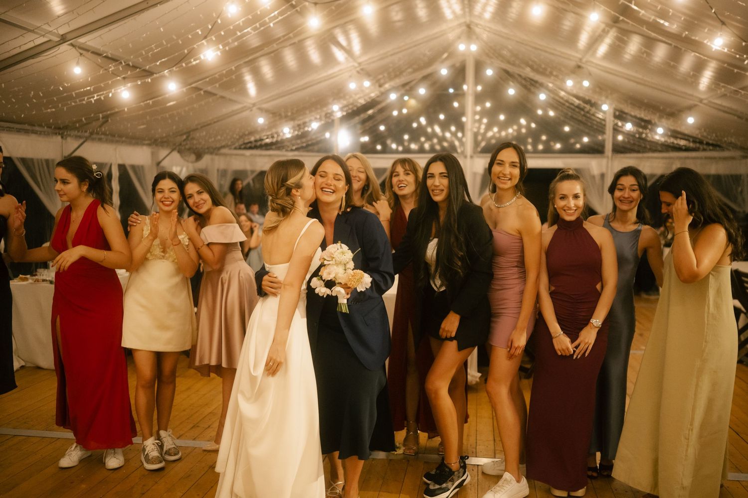 Wedding celebration with guests dancing in a tent venue decorated with string lights overhead.
