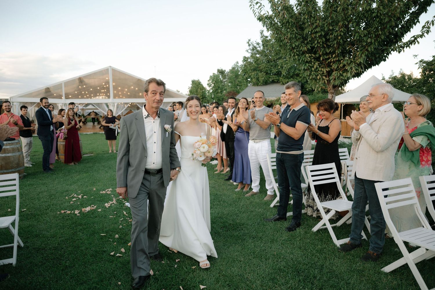 Wedding party and guests celebrate on a lush green lawn during an outdoor summer reception.