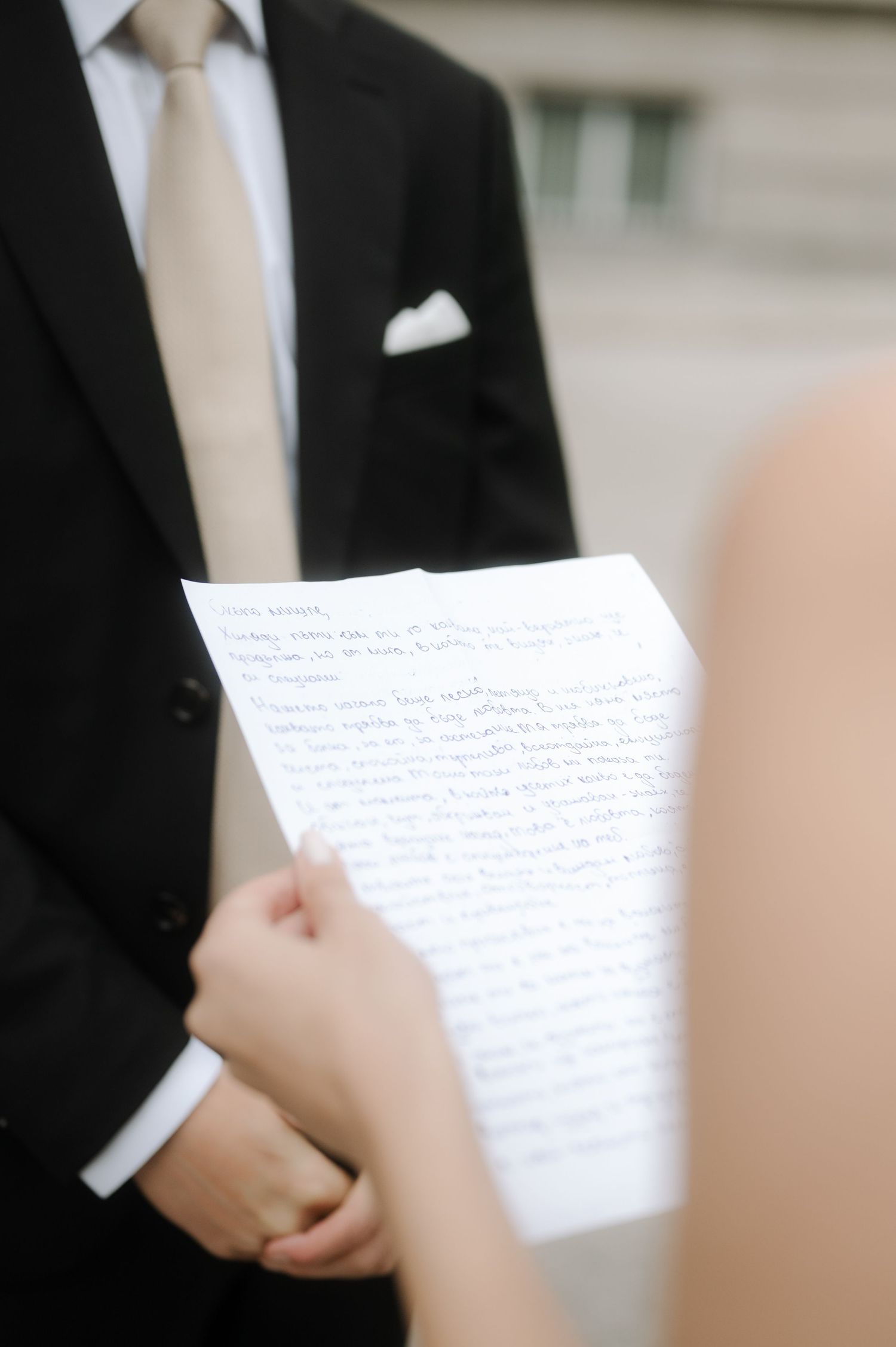 A person in a black suit and white tie holds handwritten papers during what appears to be a formal presentation.