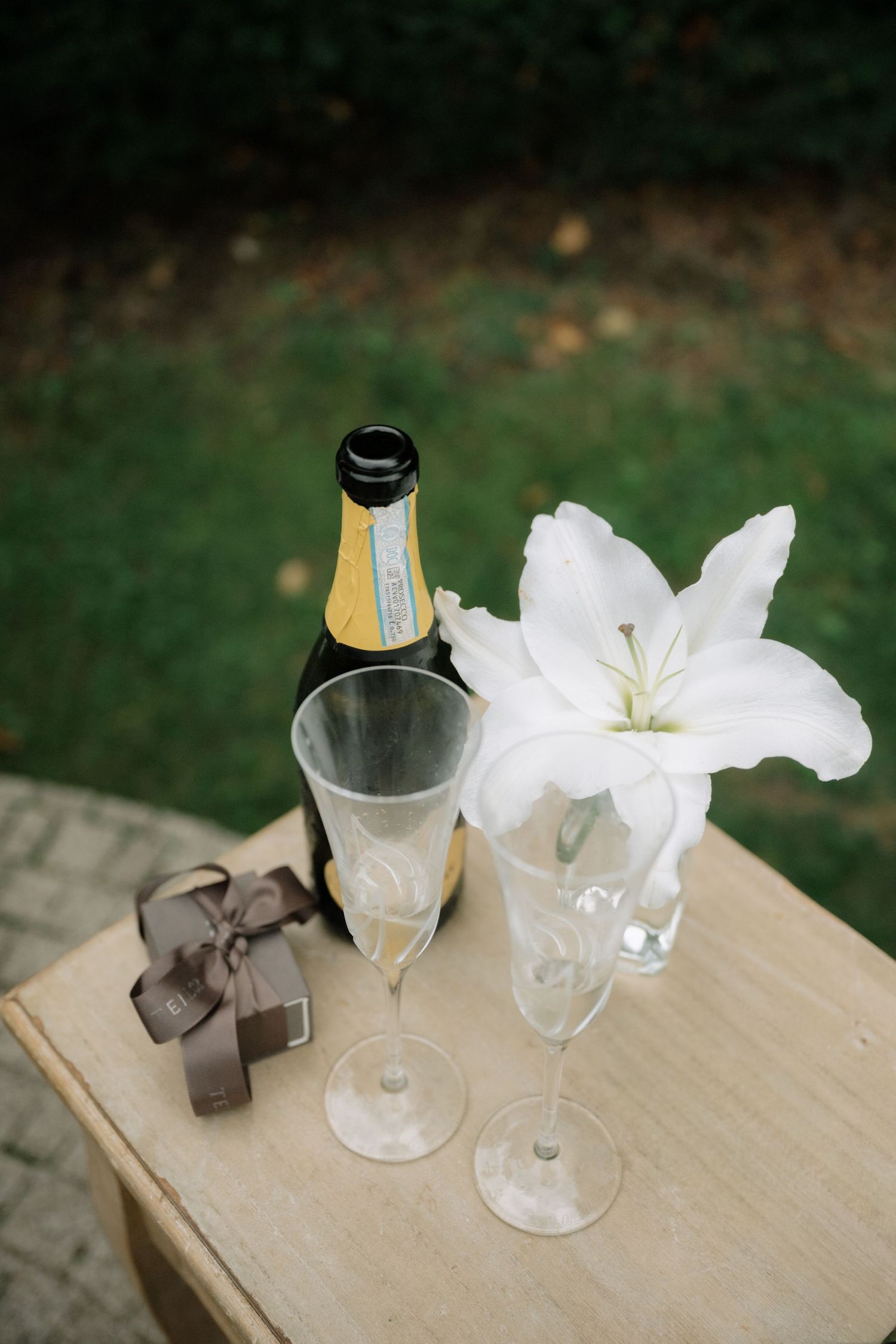 A sequence of wine glasses with white flowers and ribbons arranged on a wooden surface in a decorative display.