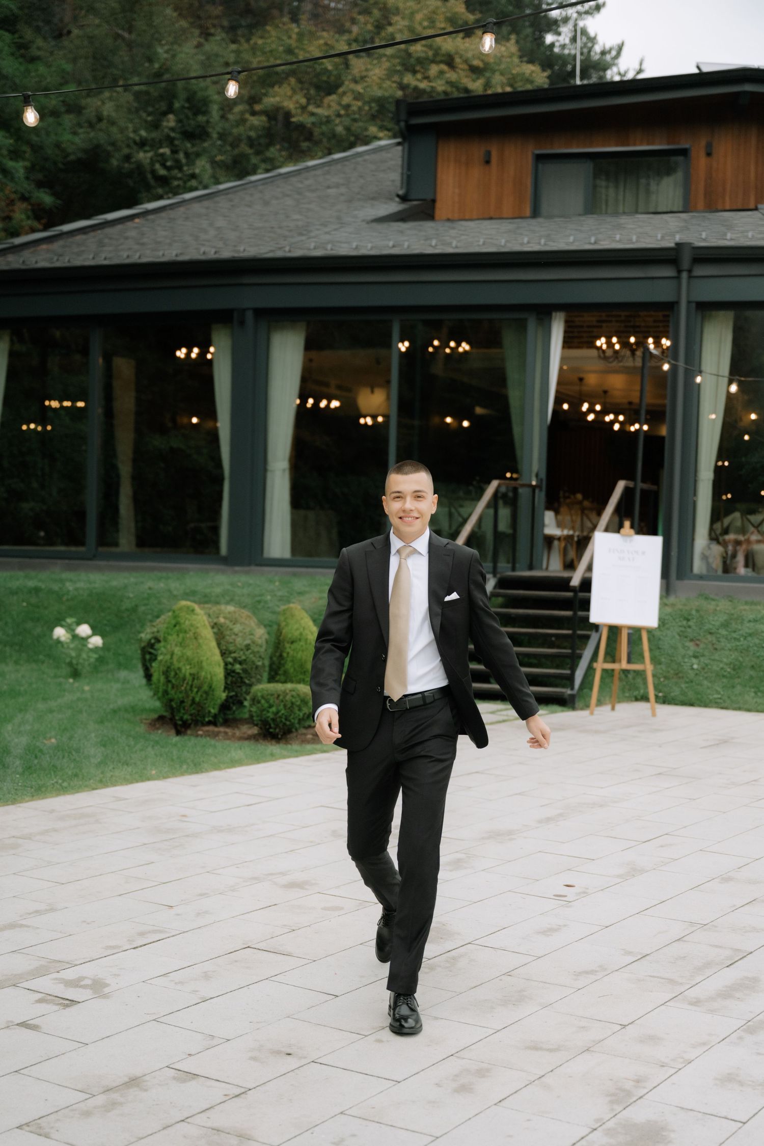 A sequence of five photos showing a person in a black suit walking across a stone patio at an outdoor venue.