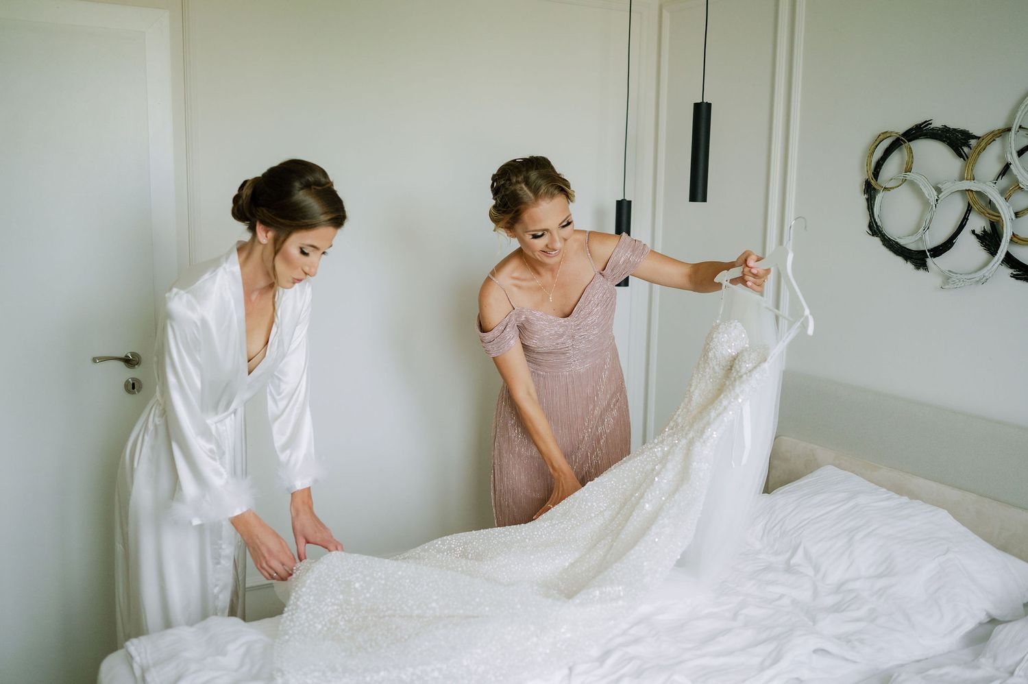People helping with wedding dress preparations in a bright room.