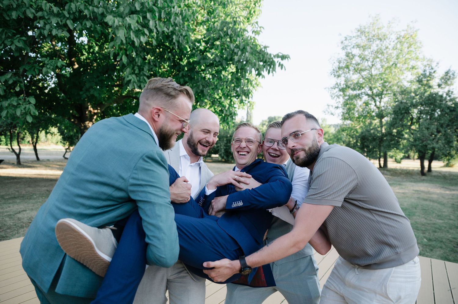 Friends in suits playfully hugging and laughing together outside.