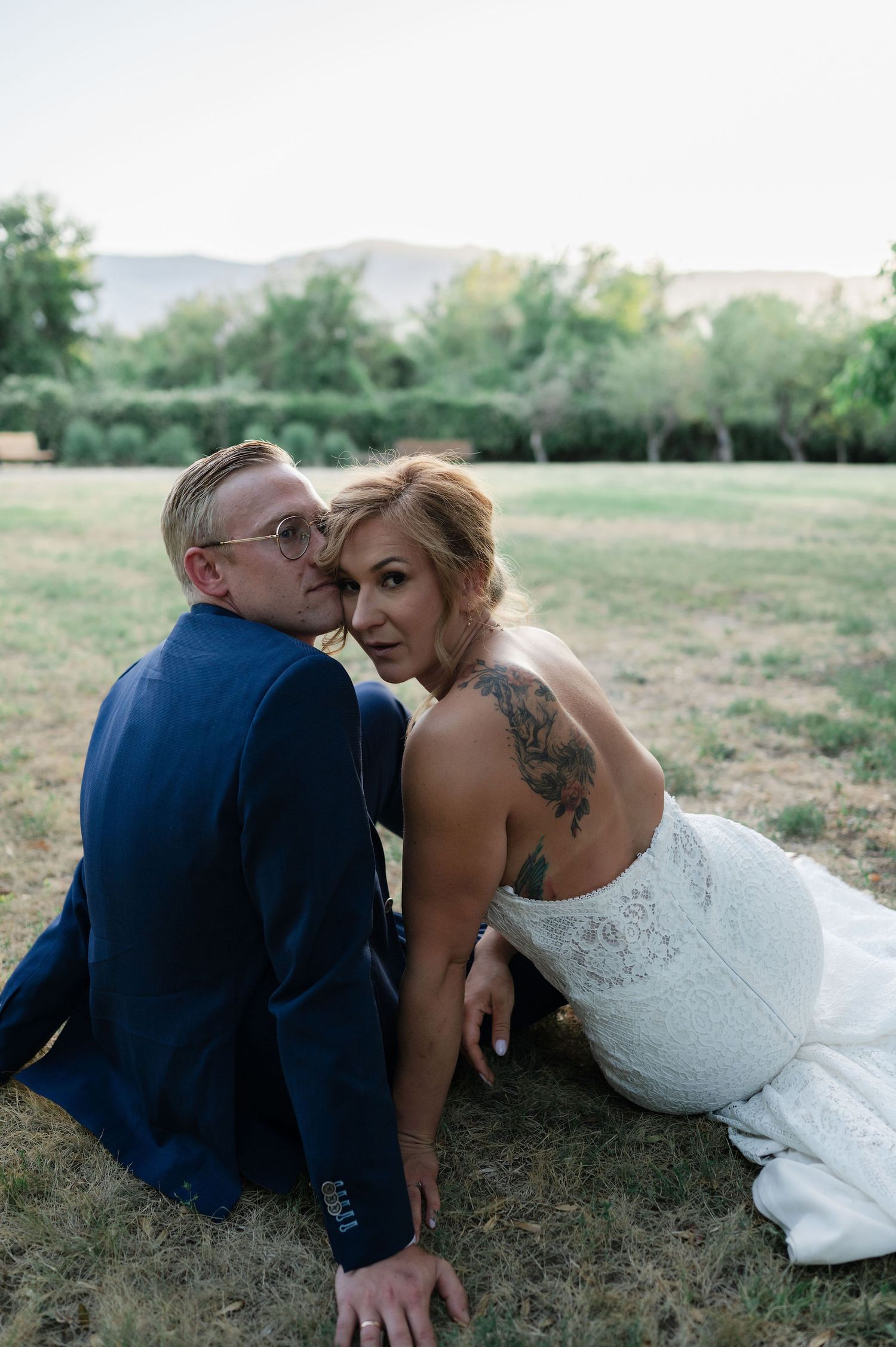 A romantic wedding couple sits together on grassy ground during an outdoor photo session.