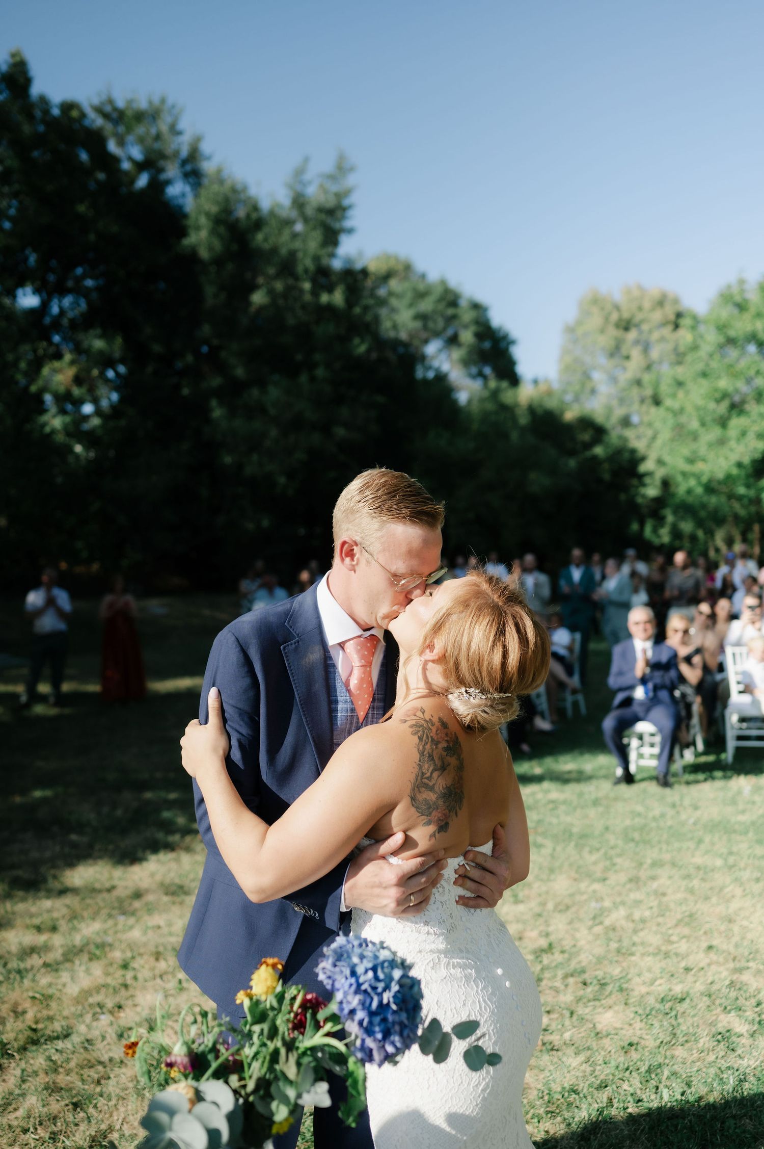 Outdoor wedding celebration with guests watching couple's first dance in garden setting.