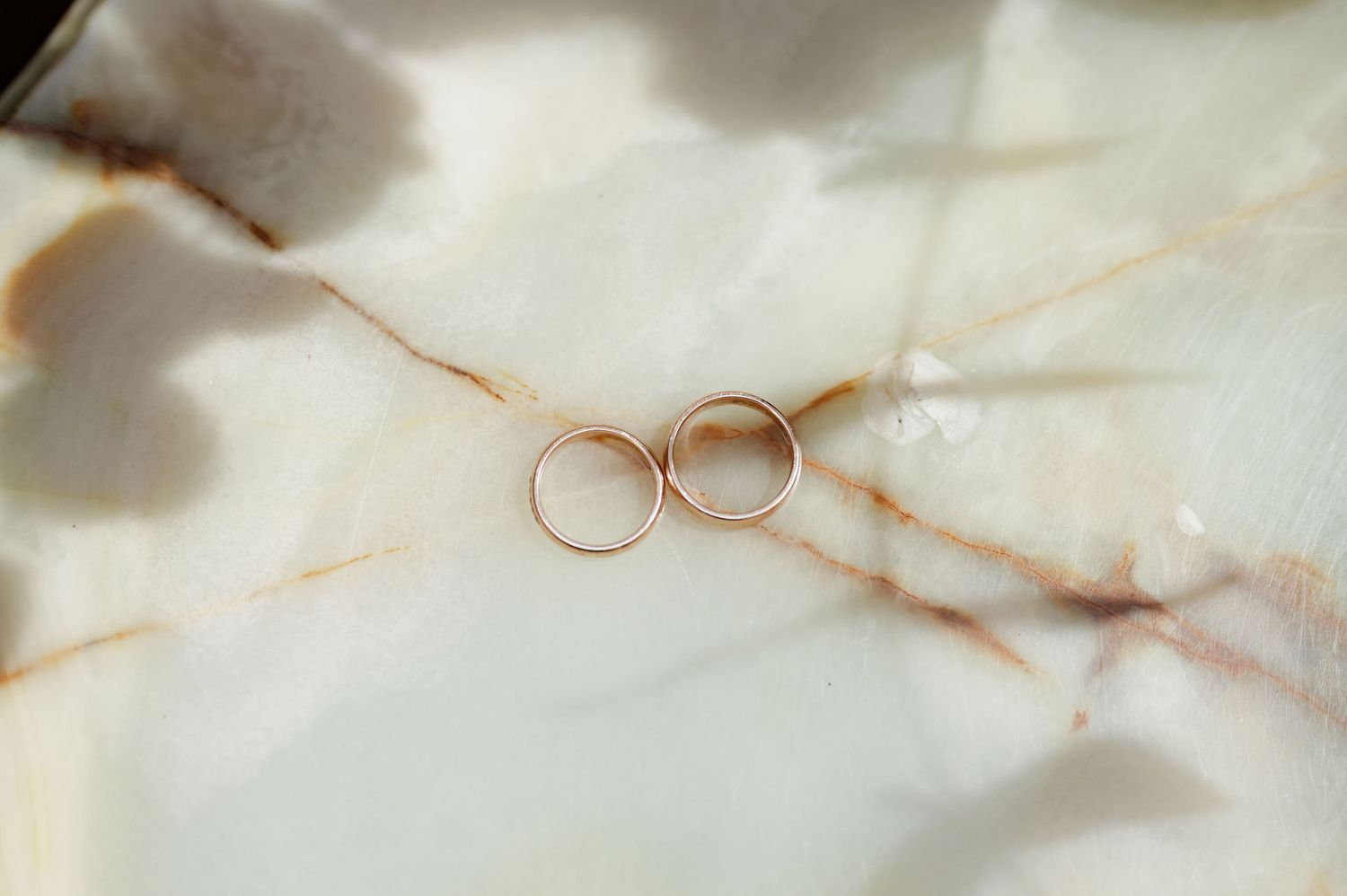 Wedding rings photographed on white marble surface with delicate veining.