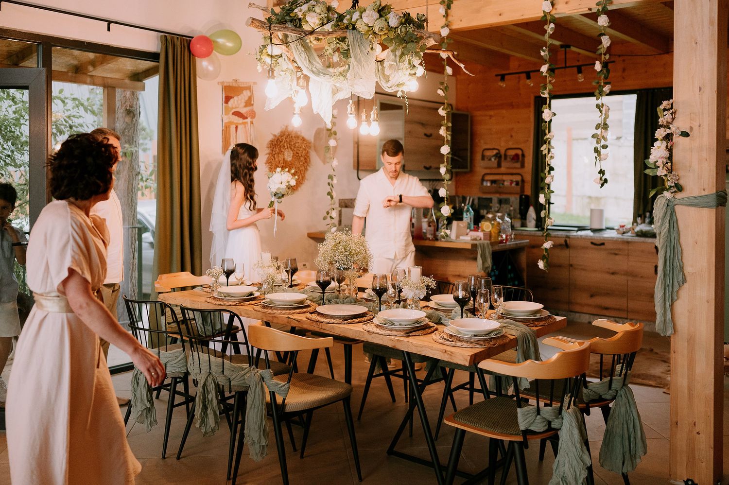 A rustic wedding reception setup with decorated wooden tables and hanging lights in a cabin-style room.