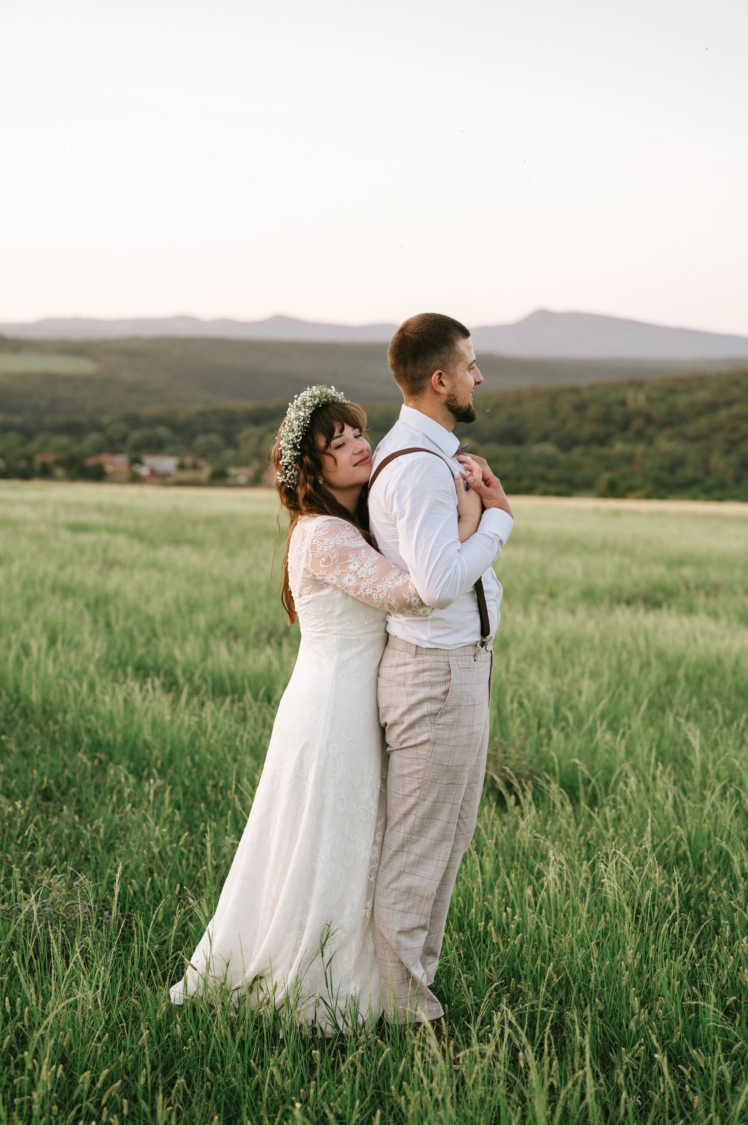 A romantic wedding portrait of a couple embracing in a grassy field with mountains in the distance.