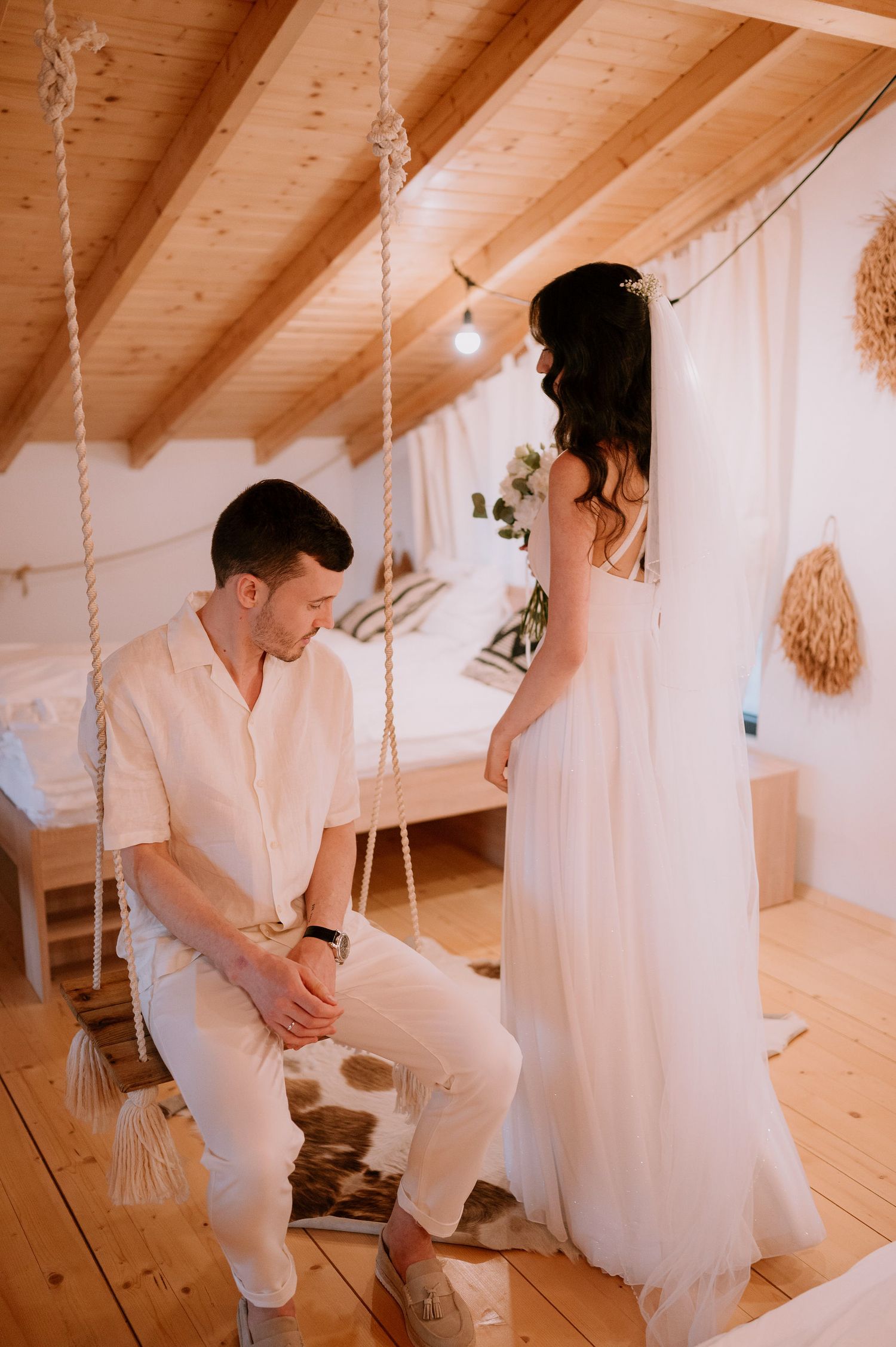 Romantic wedding scene in a rustic wooden attic room with white decor and string lights.