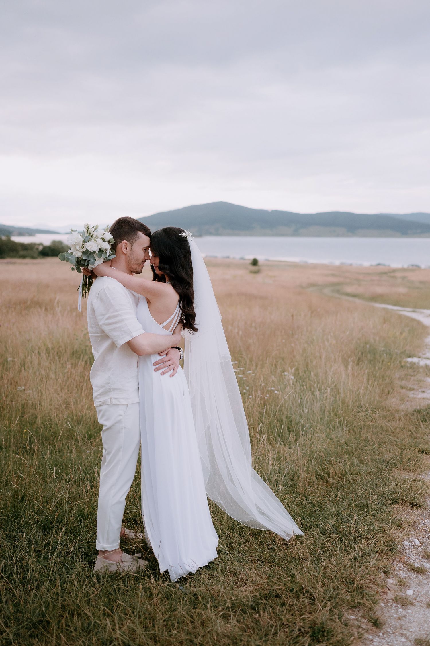 Romantic embrace between newlyweds with coastal mountains in background.