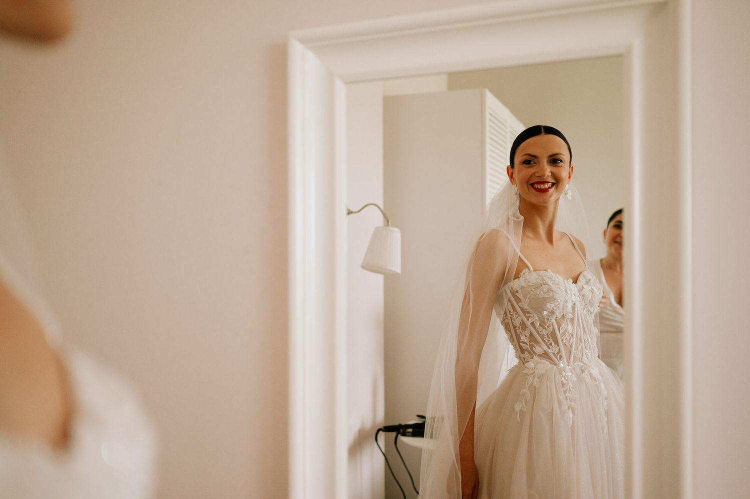 Bride in a flowing white gown stands gracefully in a sunlit room.
