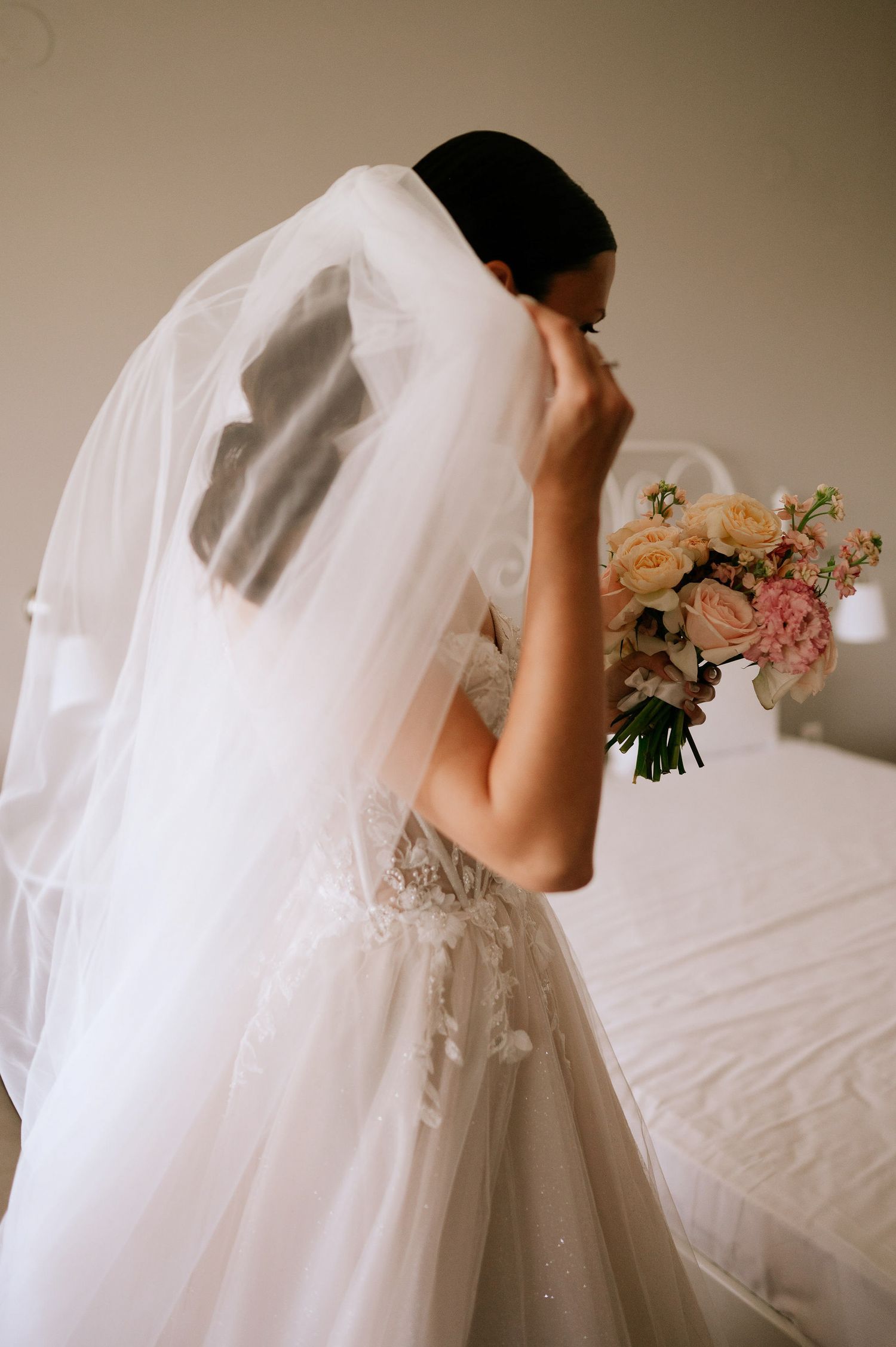 Dreamy side view of bride in flowing wedding dress holding pastel bouquet.
