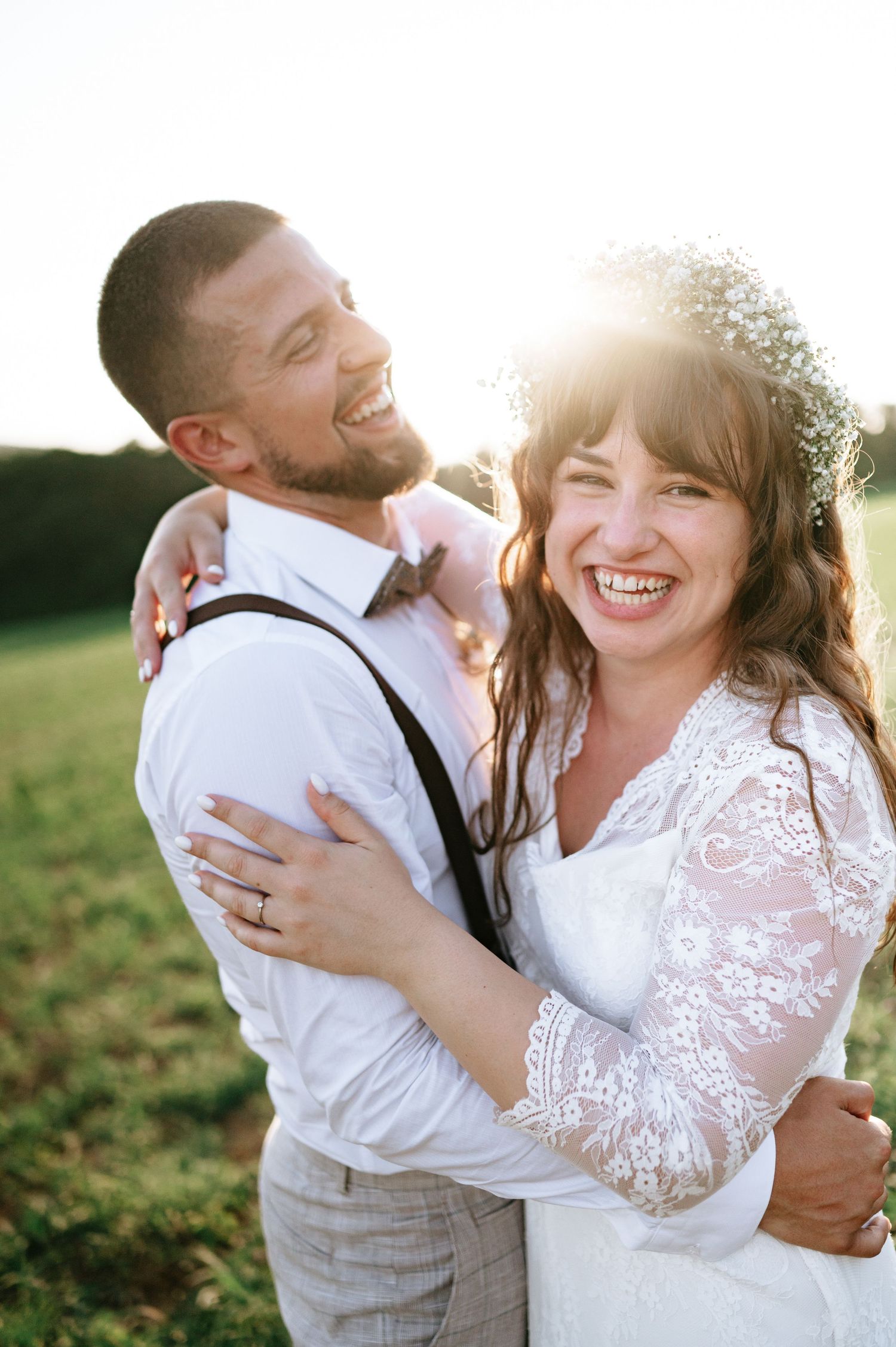 Couple shares genuine laughter during sunset wedding portraits in countryside setting.