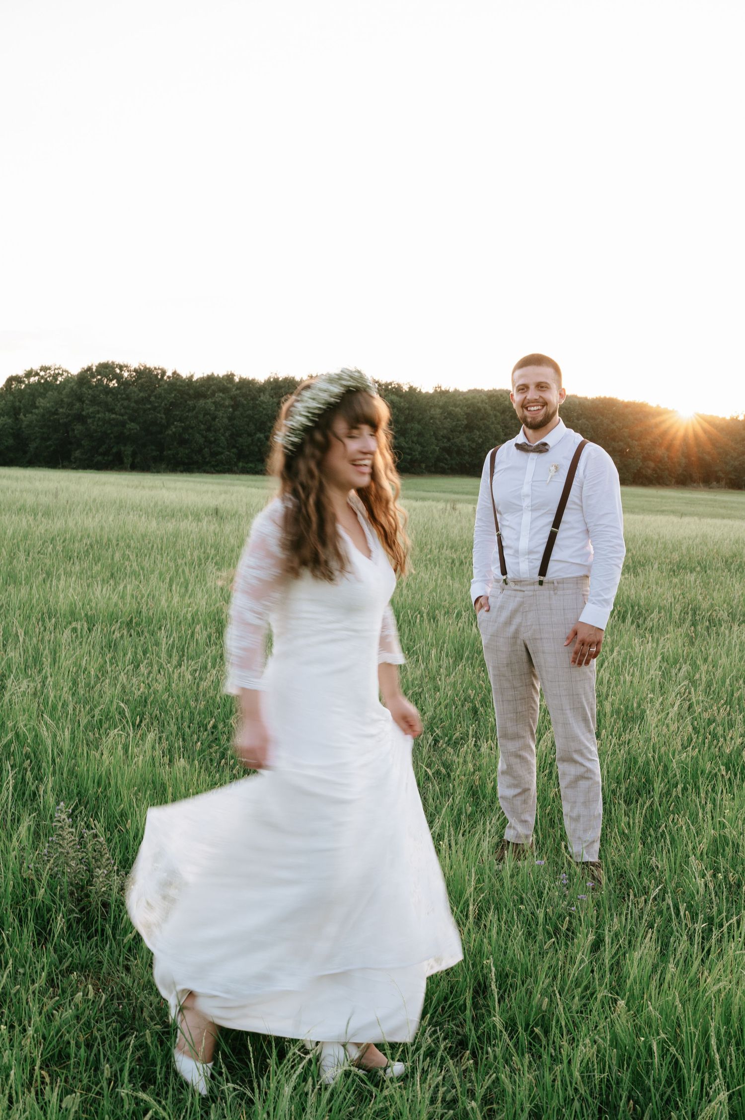 Joyful wedding couple poses playfully in a sunlit field during golden hour.