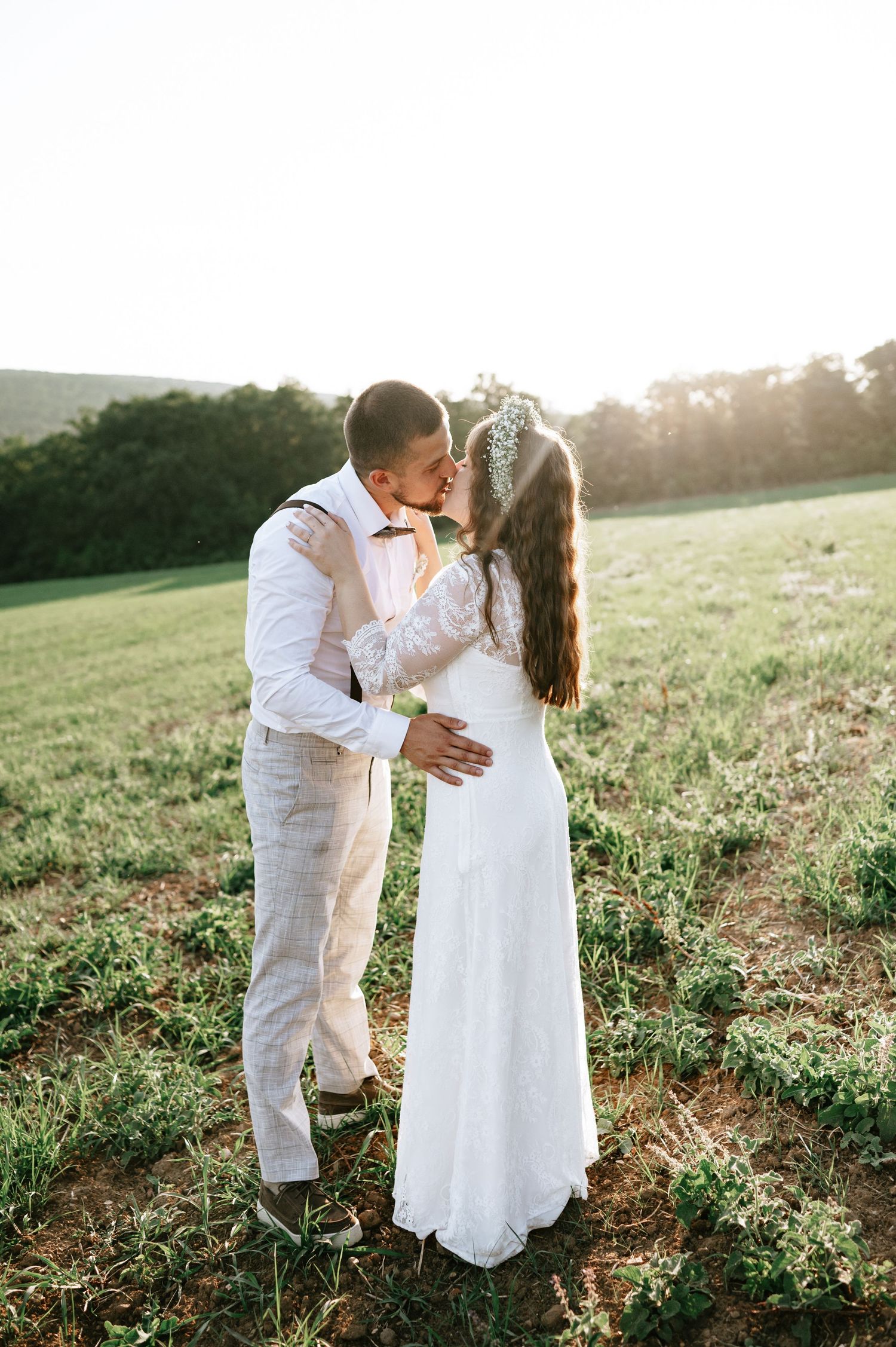 Newlyweds share tender moments in a grassy field during golden hour.