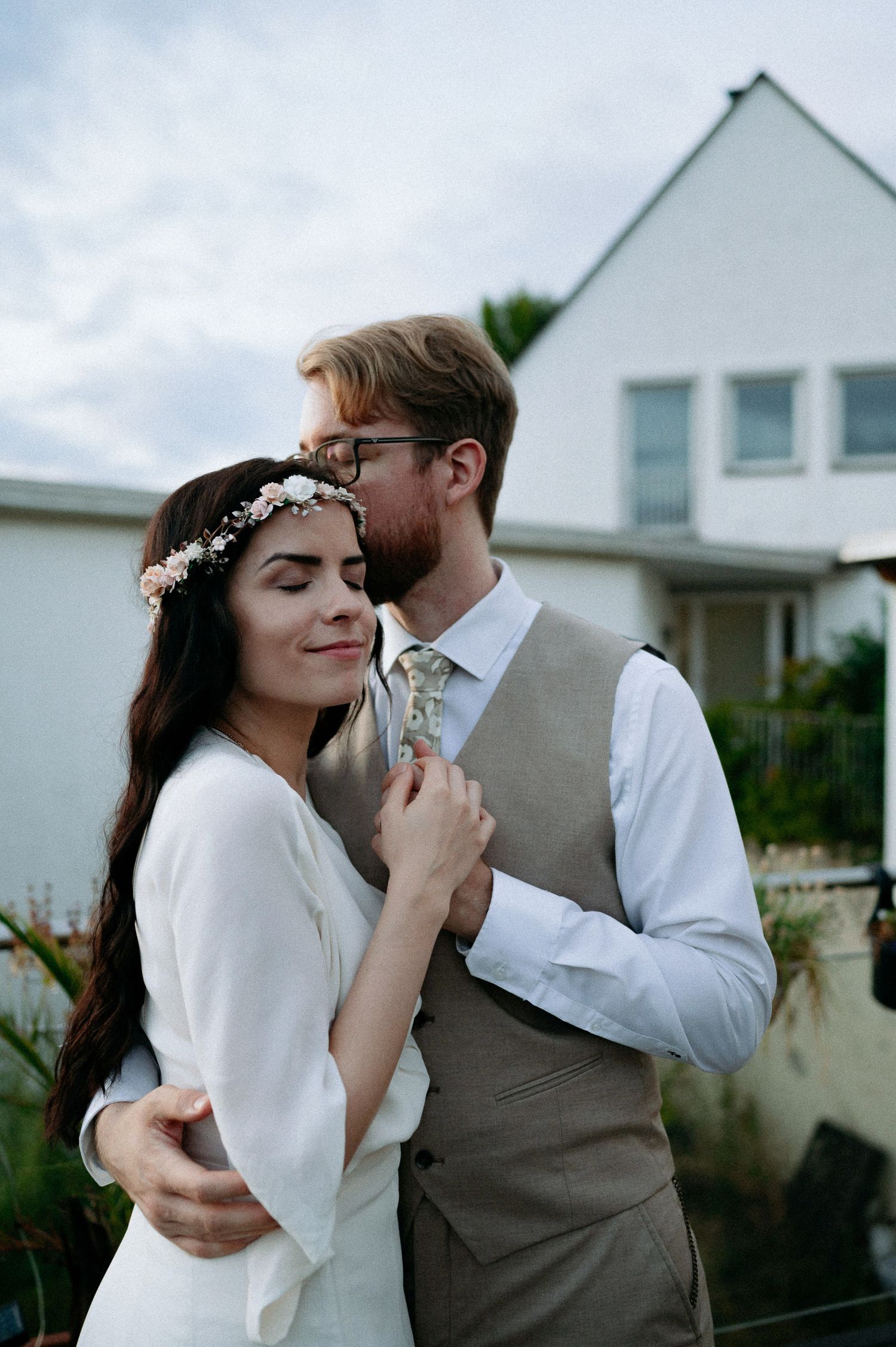 A tender moment captured against white buildings and cloudy sky.