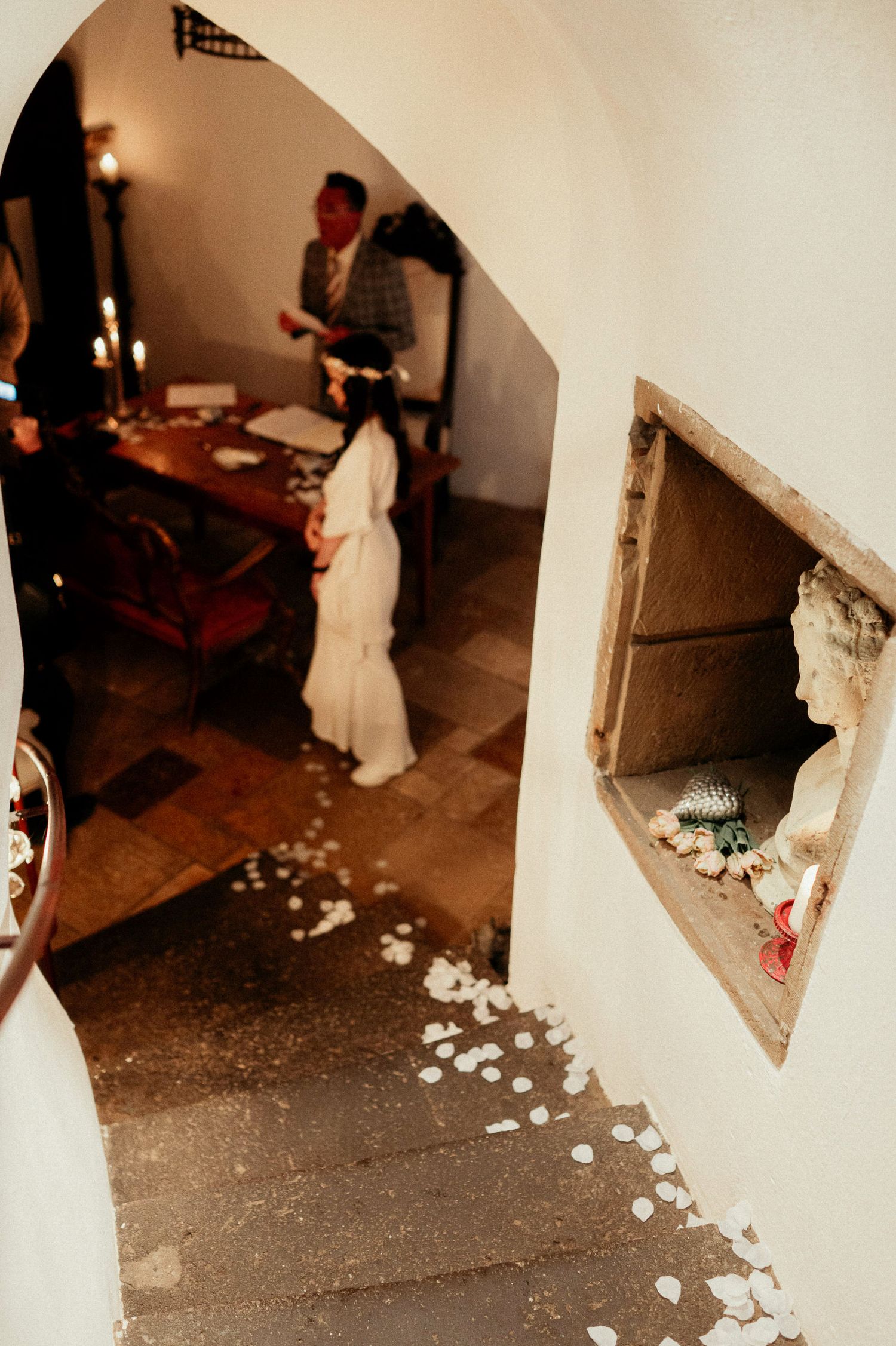Dimly lit interior hallway with white walls and scattered rose petals on the floor.