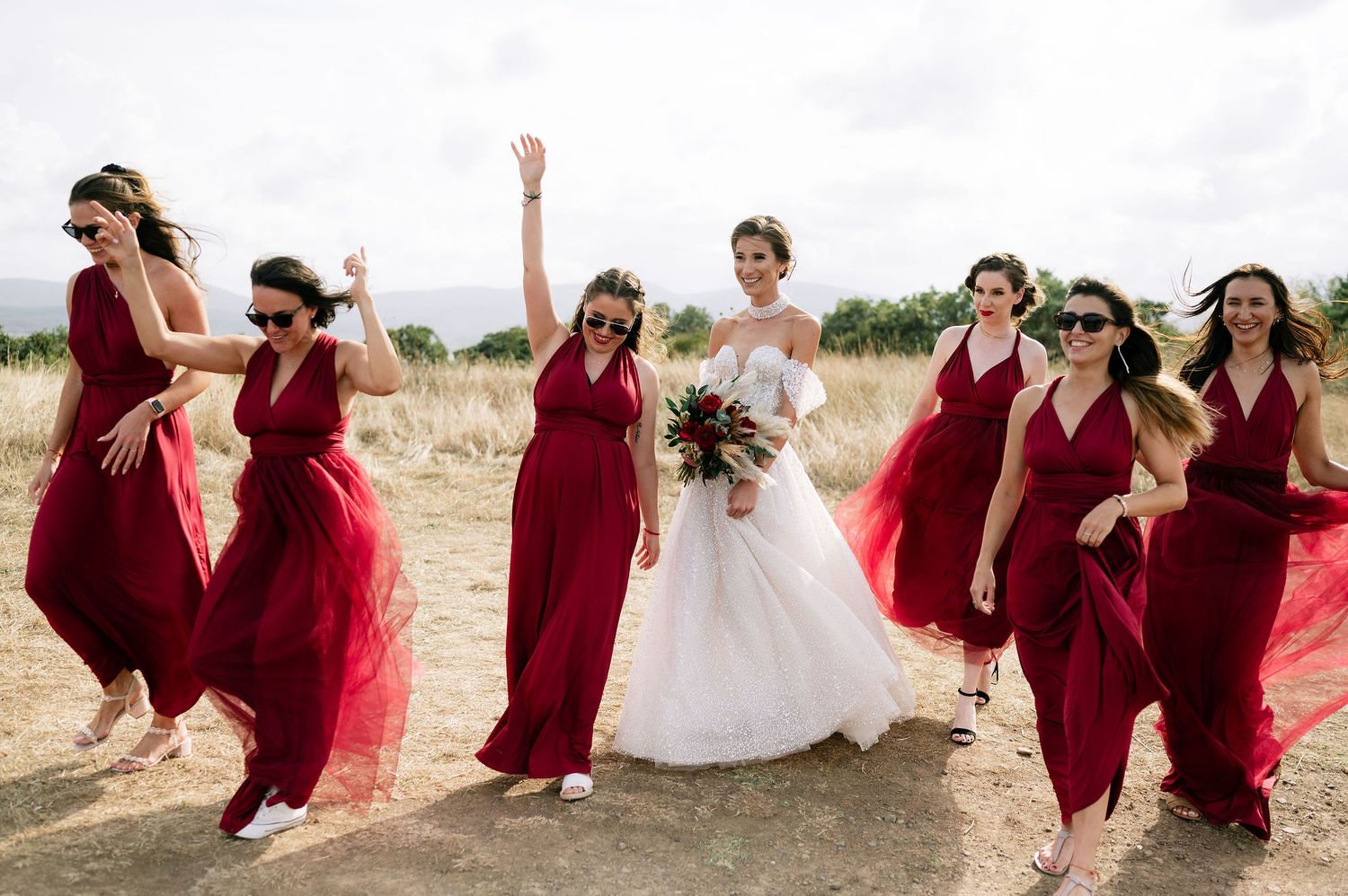 Wedding party laughing and posing together on a sunny hillside.
