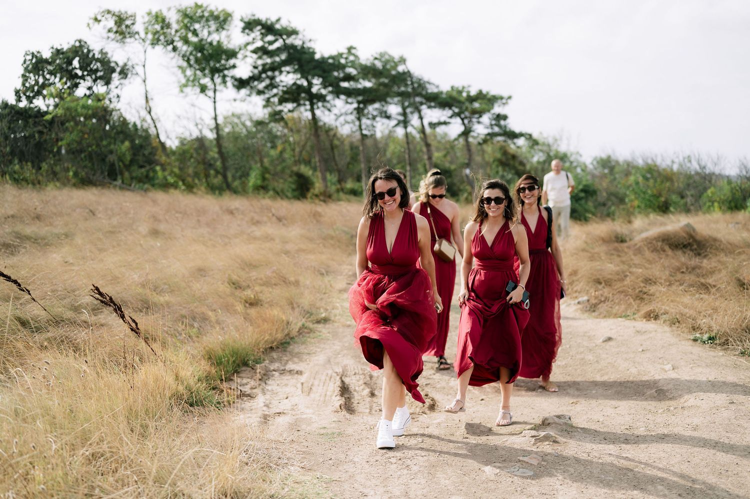 Wedding party in deep red dresses poses together on a grassy hilltop.