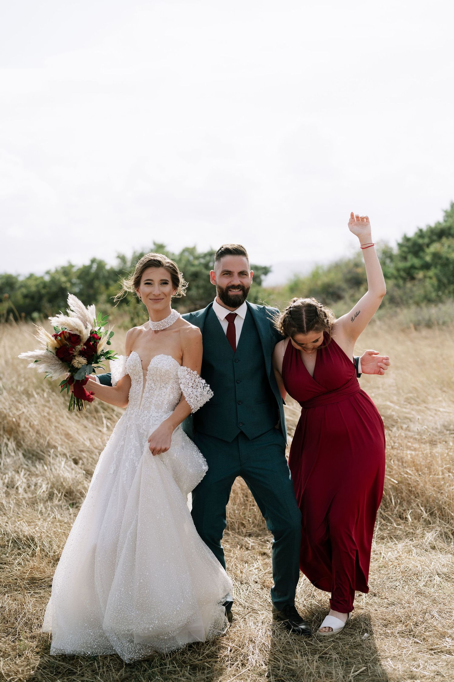 Celebratory wedding party poses together in a field with raised arms.