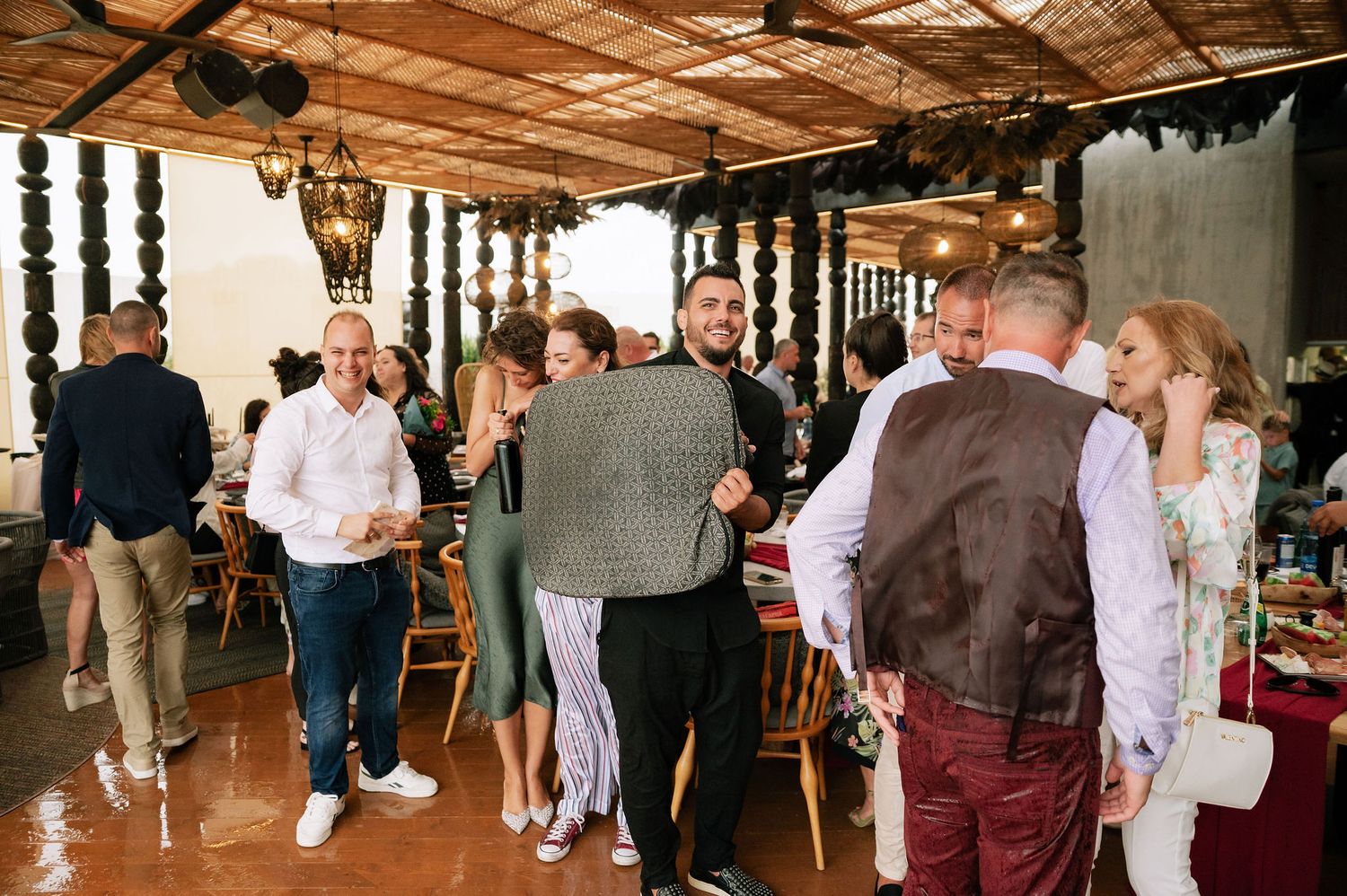 Wedding reception guests mingling in a rustic venue with wooden ceiling and hanging decorations.