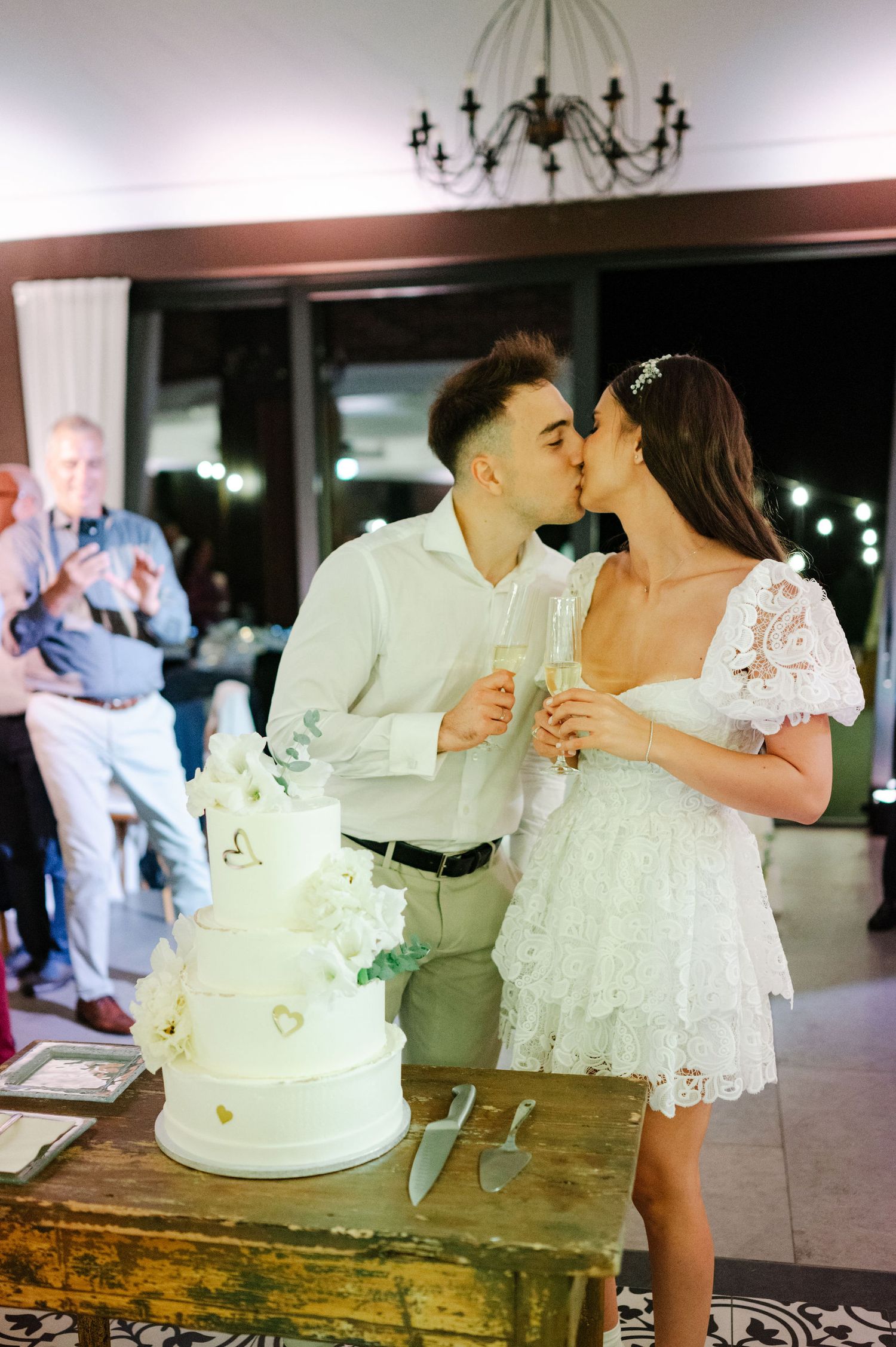 Wedding couple cutting into their elegant white tiered cake during reception celebration.