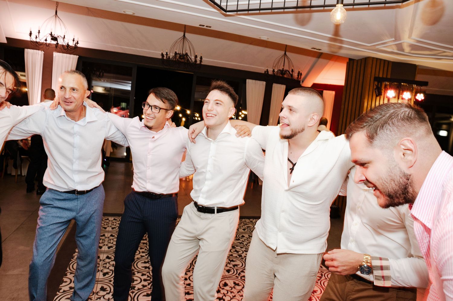 Wedding party dancing in a line formation on a patterned carpet dance floor.
