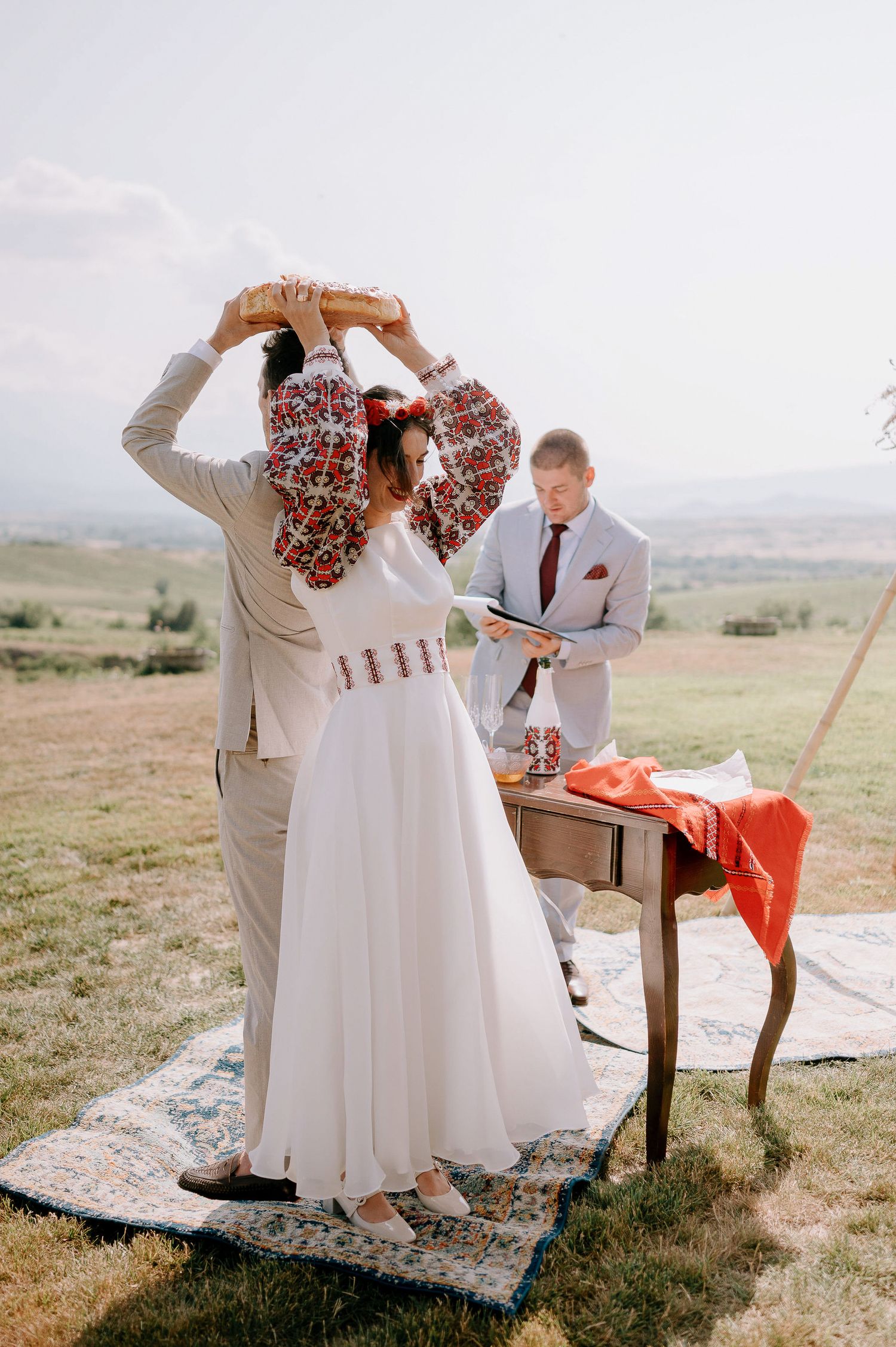 Wedding guests in light colored attire gather around a rustic table for an outdoor celebration.