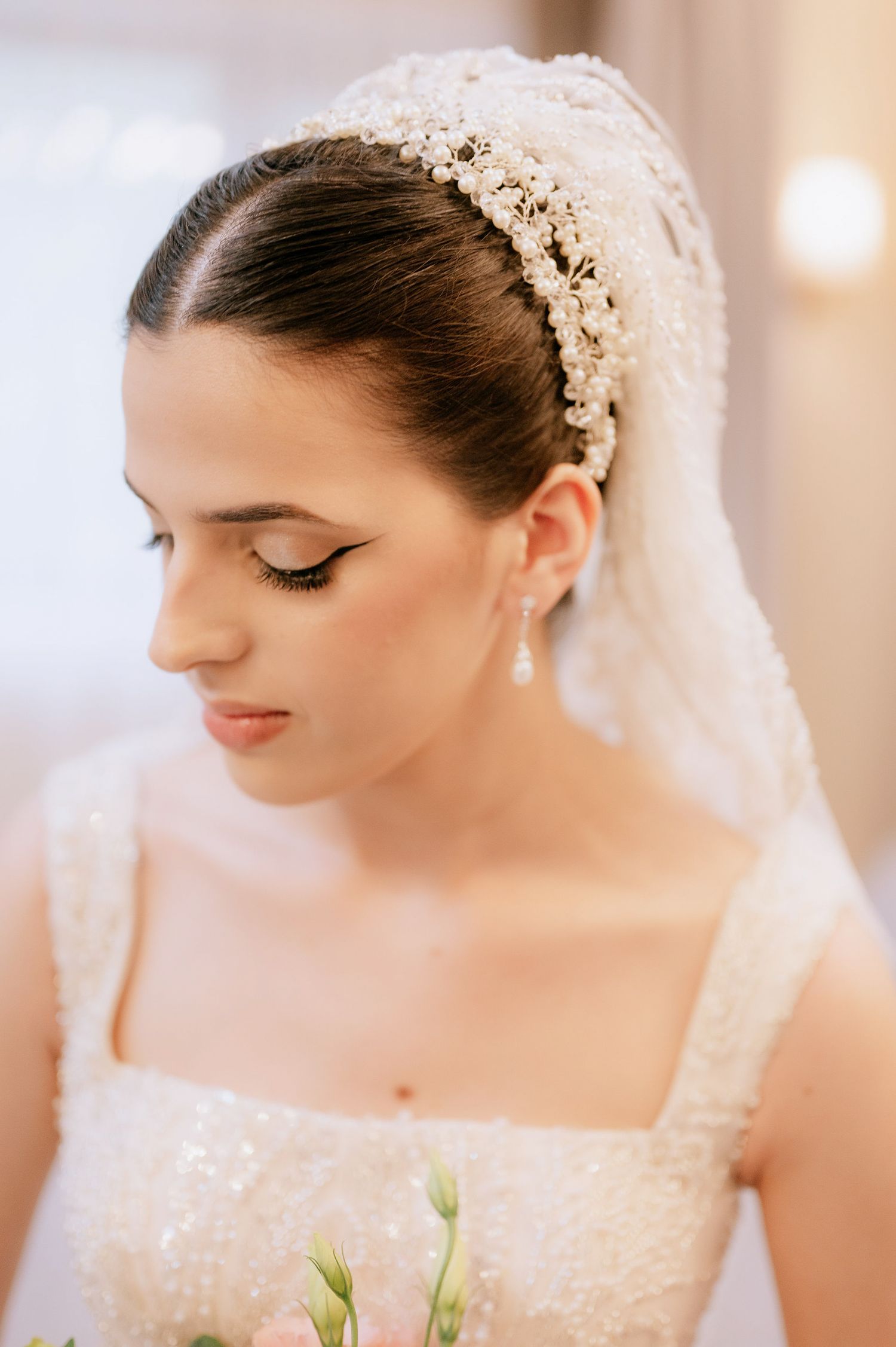 Bride wearing delicate lace veil and pearl headpiece with elegant bridal makeup and drop earrings.